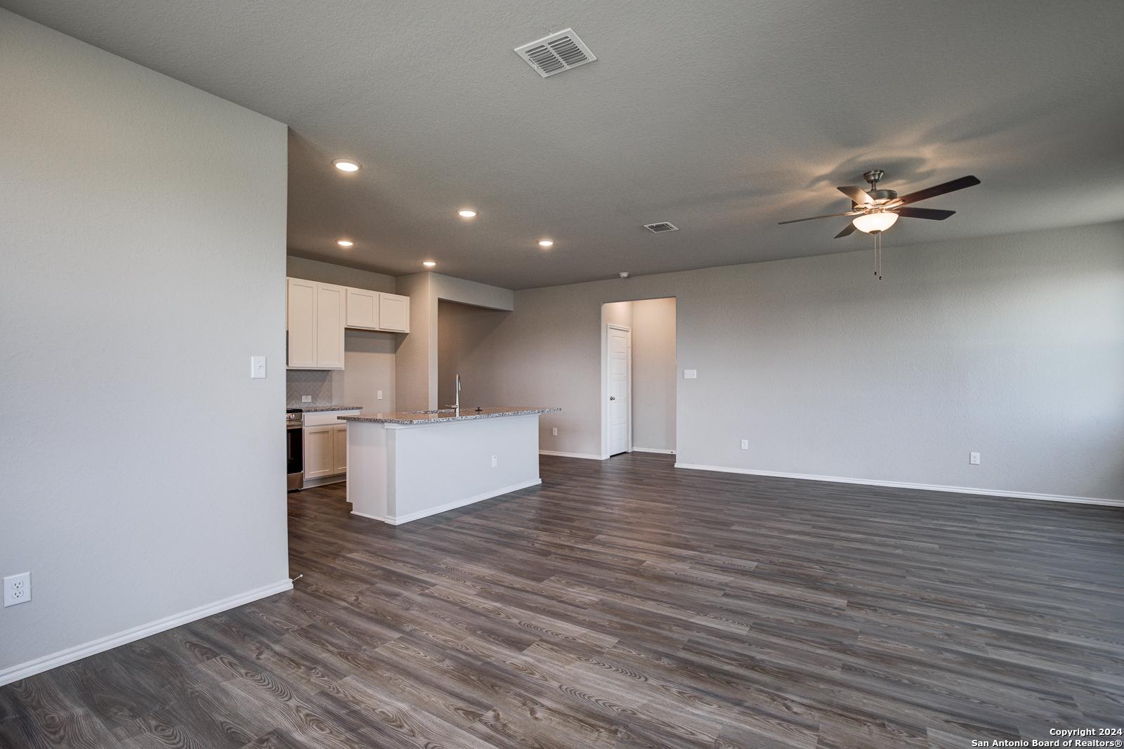 Open-concept kitchen-living area with white cabinetry, center island, ceiling fan, and laminate flooring in The Daphne J home, Seguin, Texas