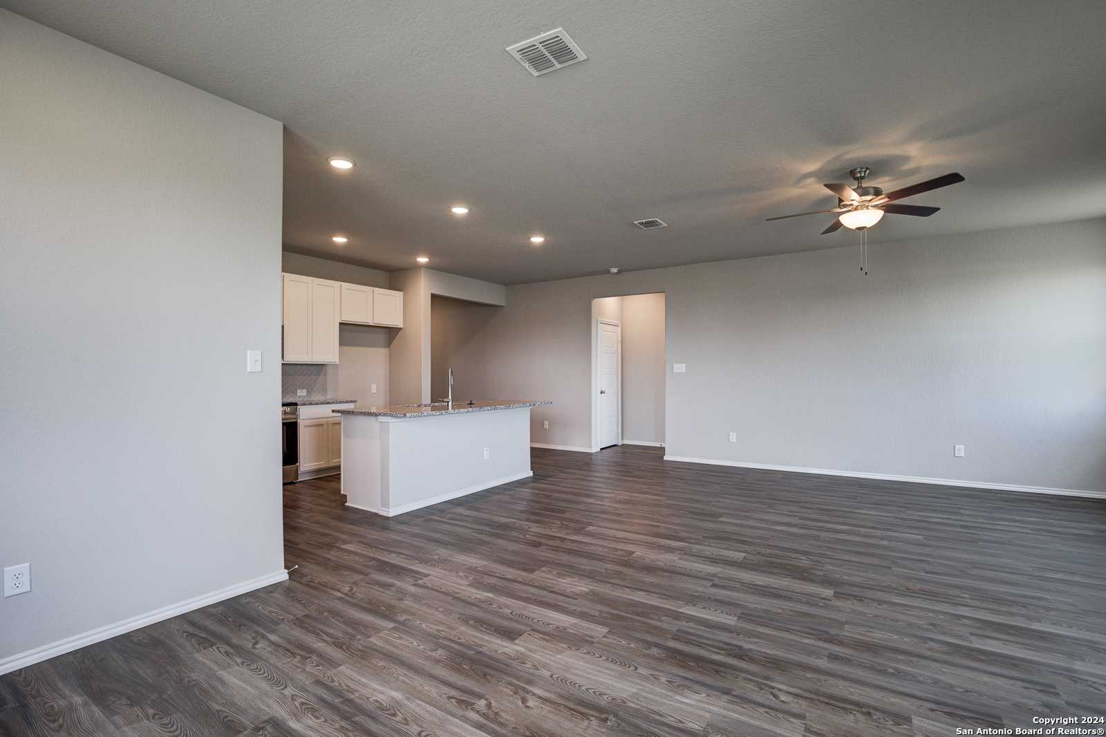 Open-concept kitchen-living area with white cabinetry, center island, ceiling fan, and laminate flooring in The Daphne J home, Seguin, Texas