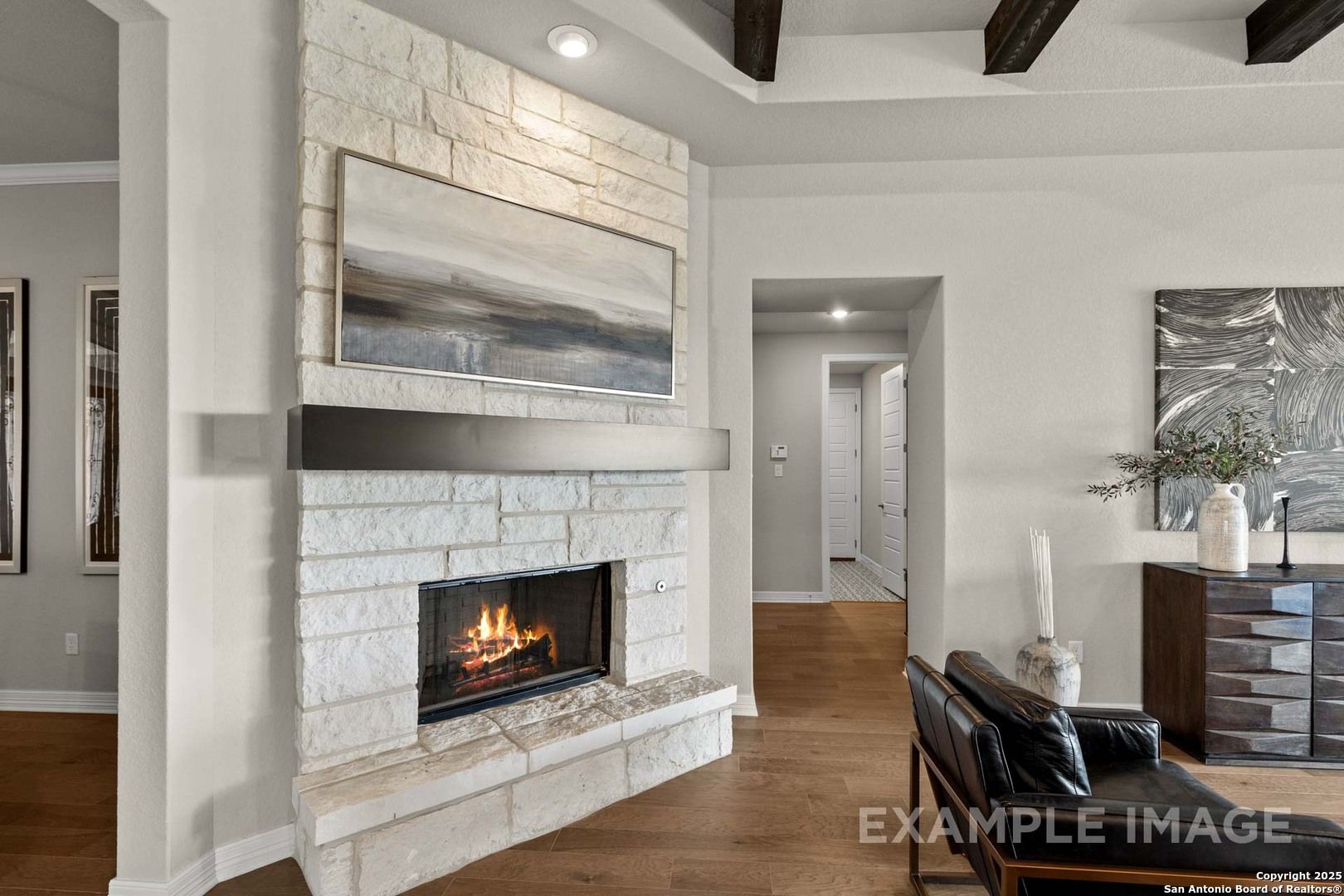 Elegant stone fireplace with flames in open living room, wooden beam ceiling, abstract art, Davidson Homes The Summerlin B, Castroville TX