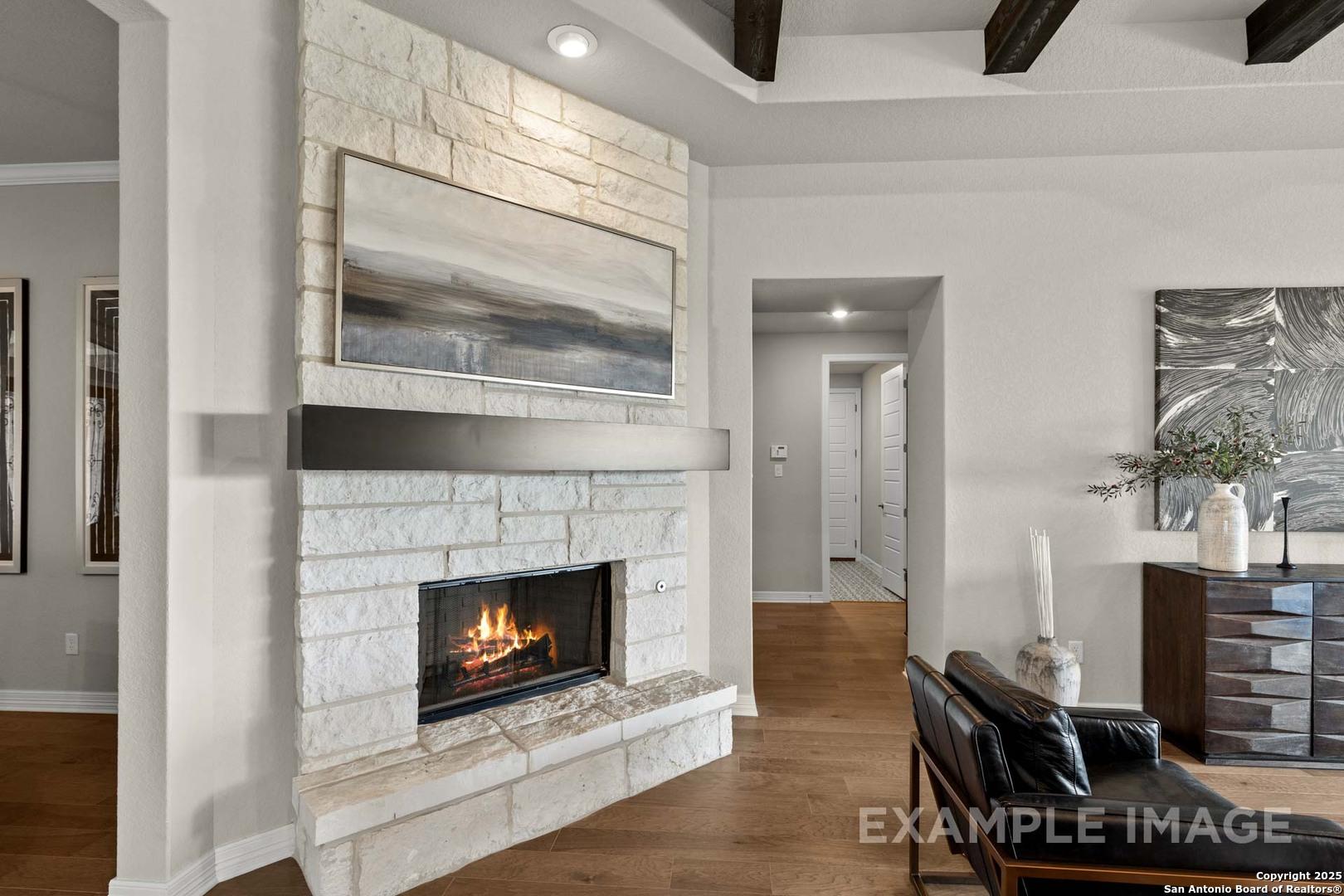Elegant stone fireplace with flames in open living room, wooden beam ceiling, abstract art, Davidson Homes The Summerlin B, Castroville TX
