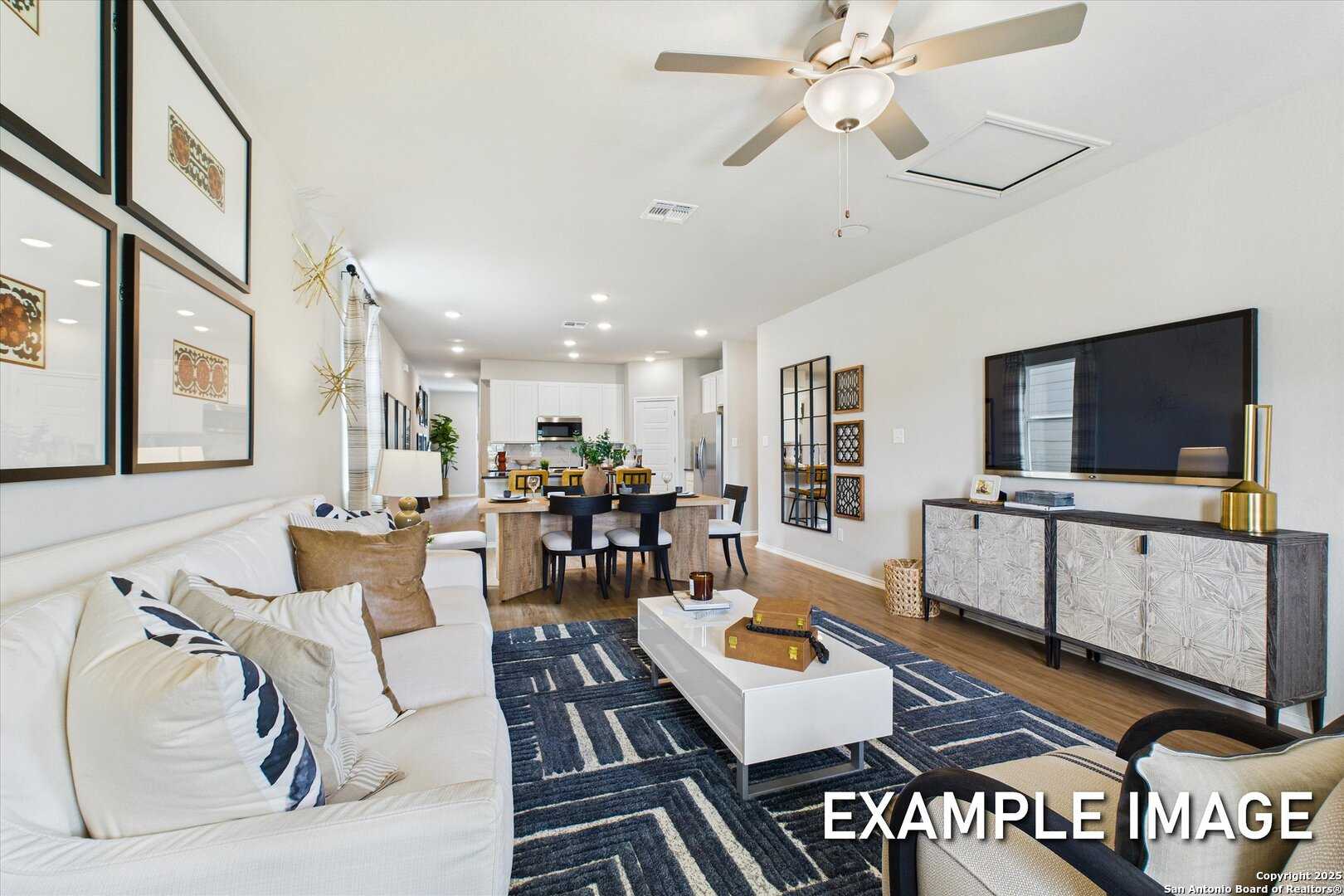 Modern open-concept living and dining area with white sofa, wooden table, kitchen in Davidson Homes The Sabine C, San Antonio