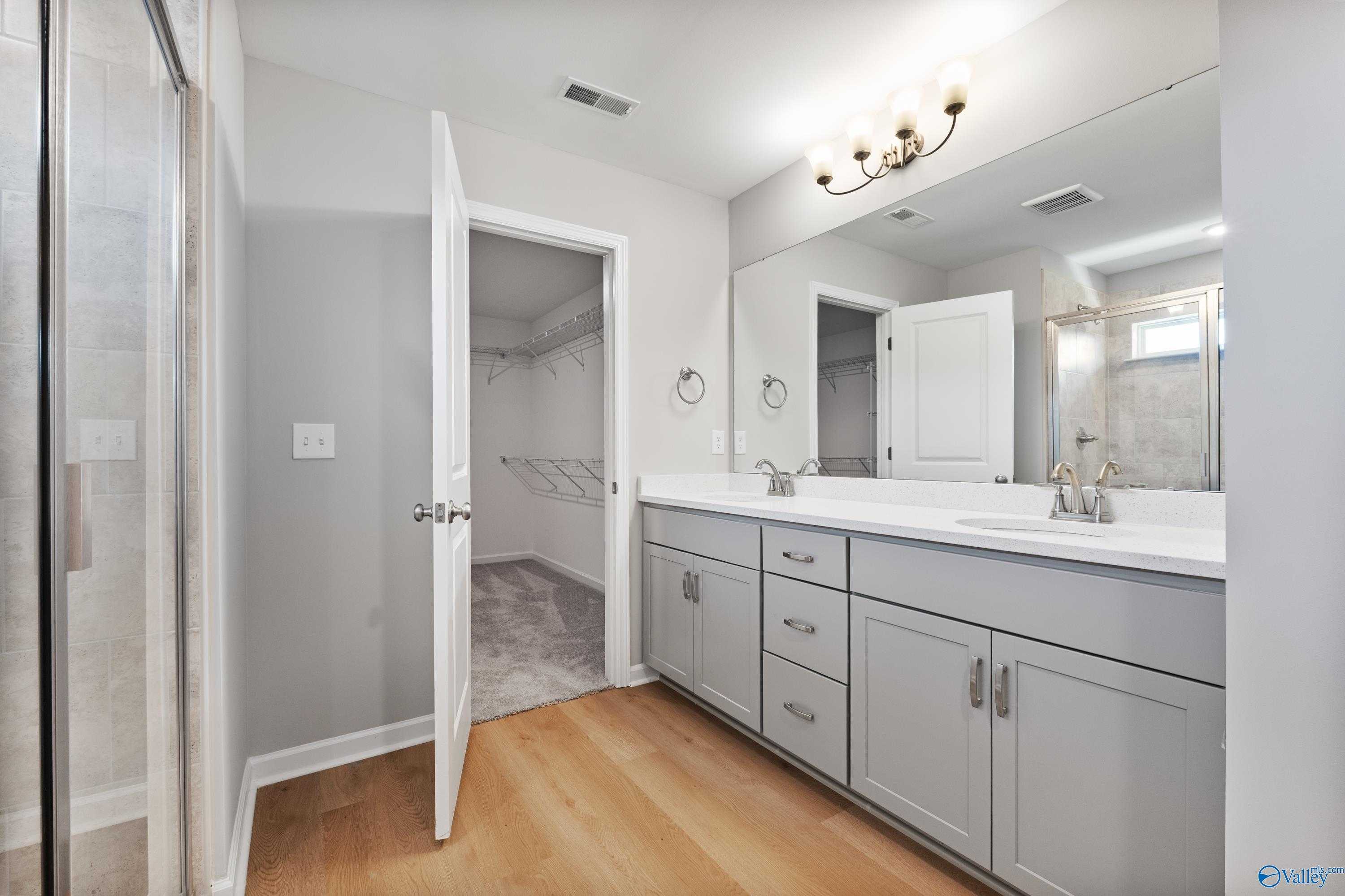 Modern master bathroom featuring double gray vanity, mirrors, chandelier, and open walk-in closet in Davidson Homes The Charm, Huntsville, Alabama