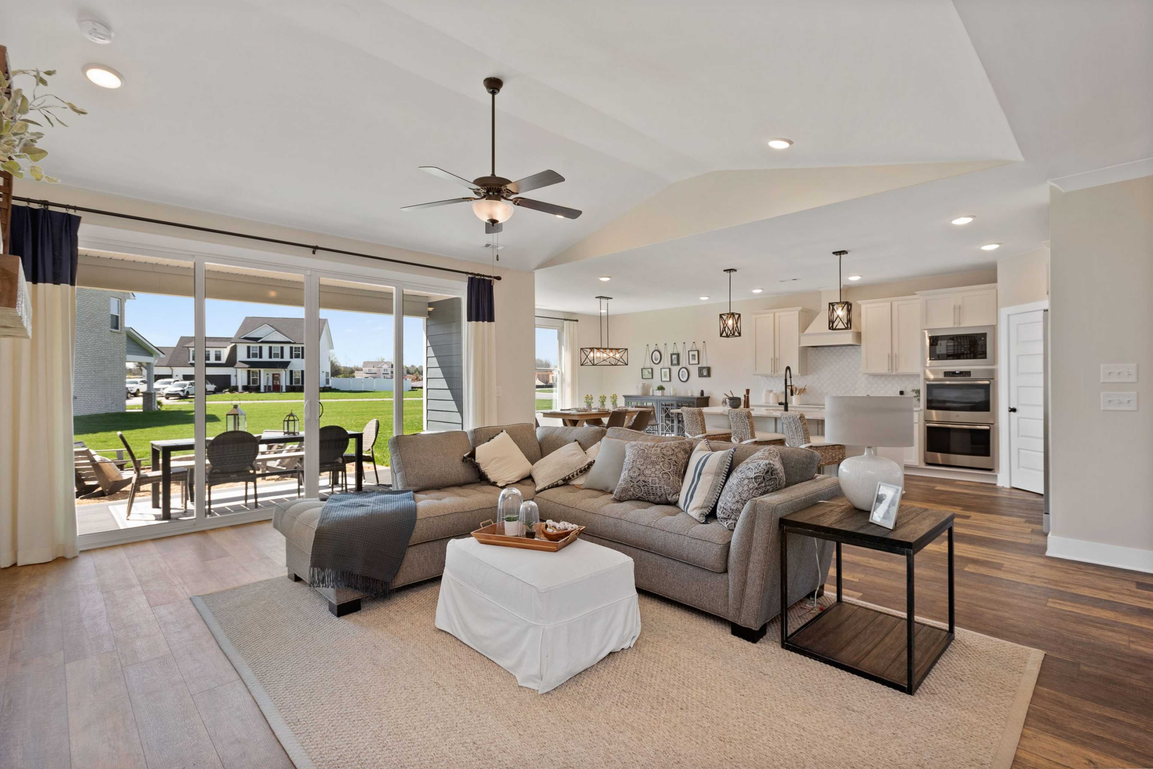 Spacious open-concept living room and kitchen in Rivers Edge Murfreesboro TN with hardwood floors, gray sectional sofa, and sliding doors to backyard pool