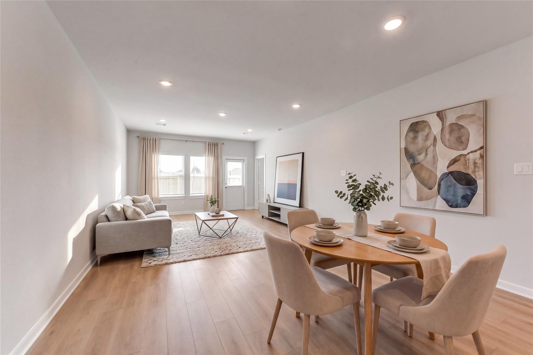 Bright open-concept living and dining space with gray sofa, oak table, beige chairs, and large windows in Davidson Homes The Sabine F, Dayton, Texas