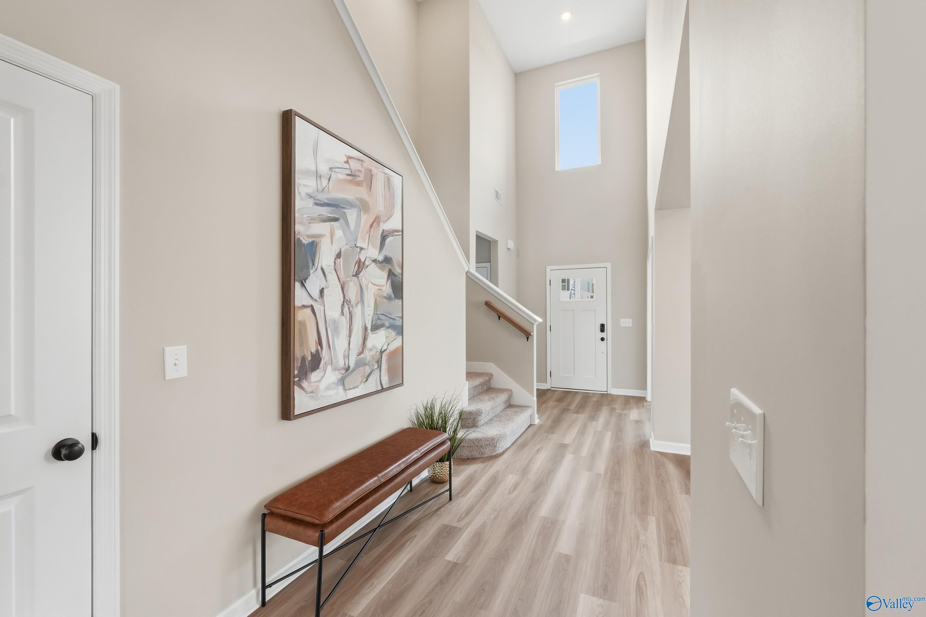 Elegant two-story foyer with grand staircase, abstract wall art, leather bench, and LVP flooring in Davidson Homes The Dorado, Huntsville AL