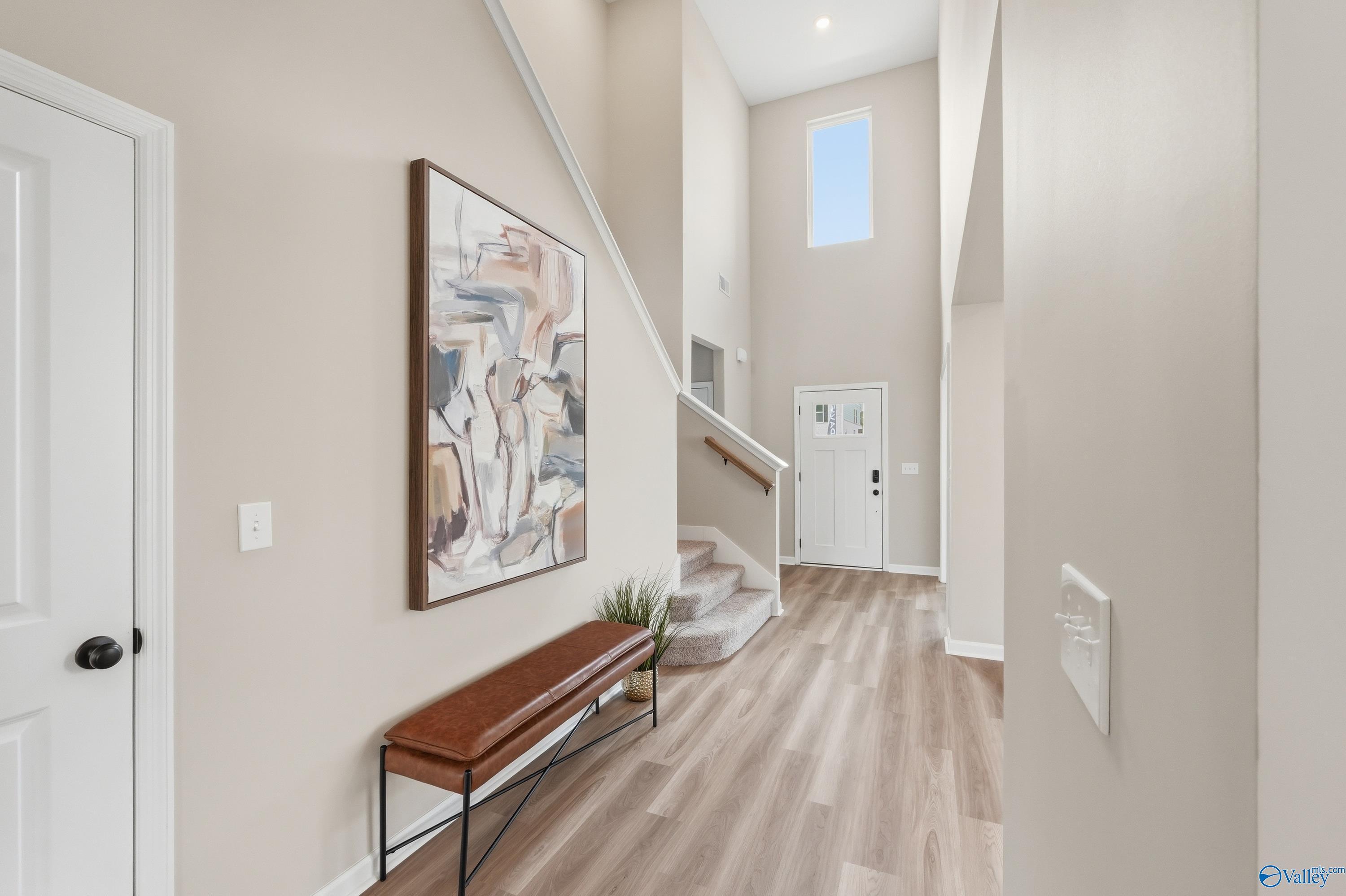 Elegant two-story foyer with grand staircase, abstract wall art, leather bench, and LVP flooring in Davidson Homes The Dorado, Huntsville AL