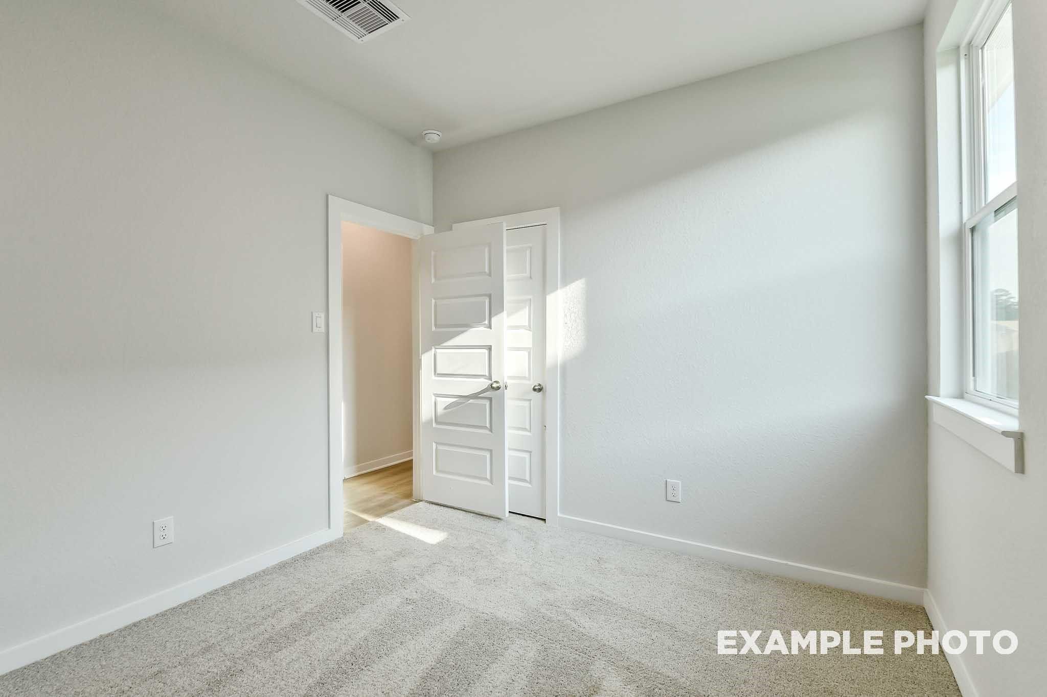 Bright secondary bedroom with light gray walls, beige carpet, open closet door, and large window in Davidson Homes The Colorado G, Conroe, Texas