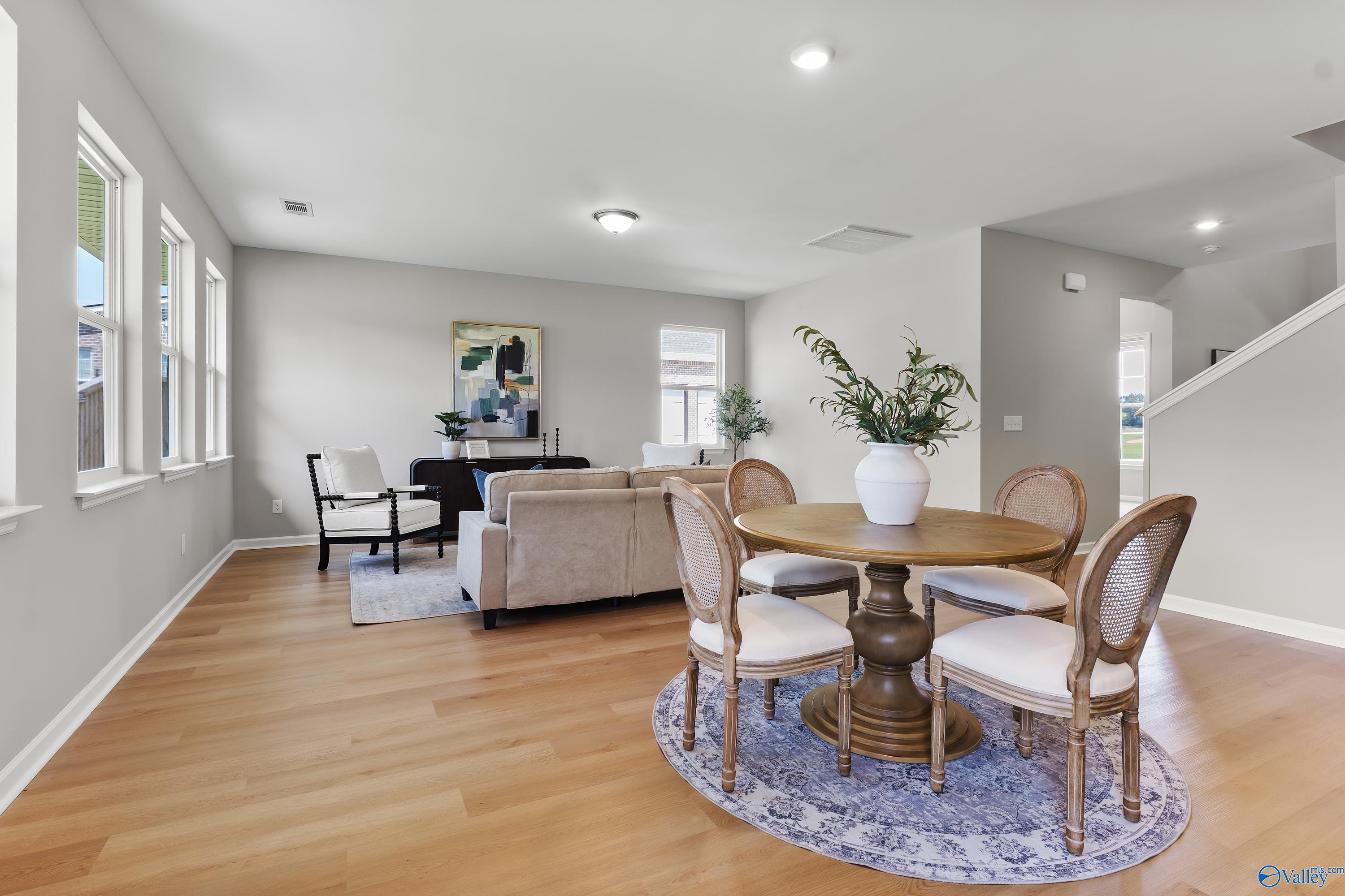 Elegant open living space with beige sofa, round wood pedestal table, upholstered chairs, and hardwood floors in Davidson Homes The Charm, Huntsville AL
