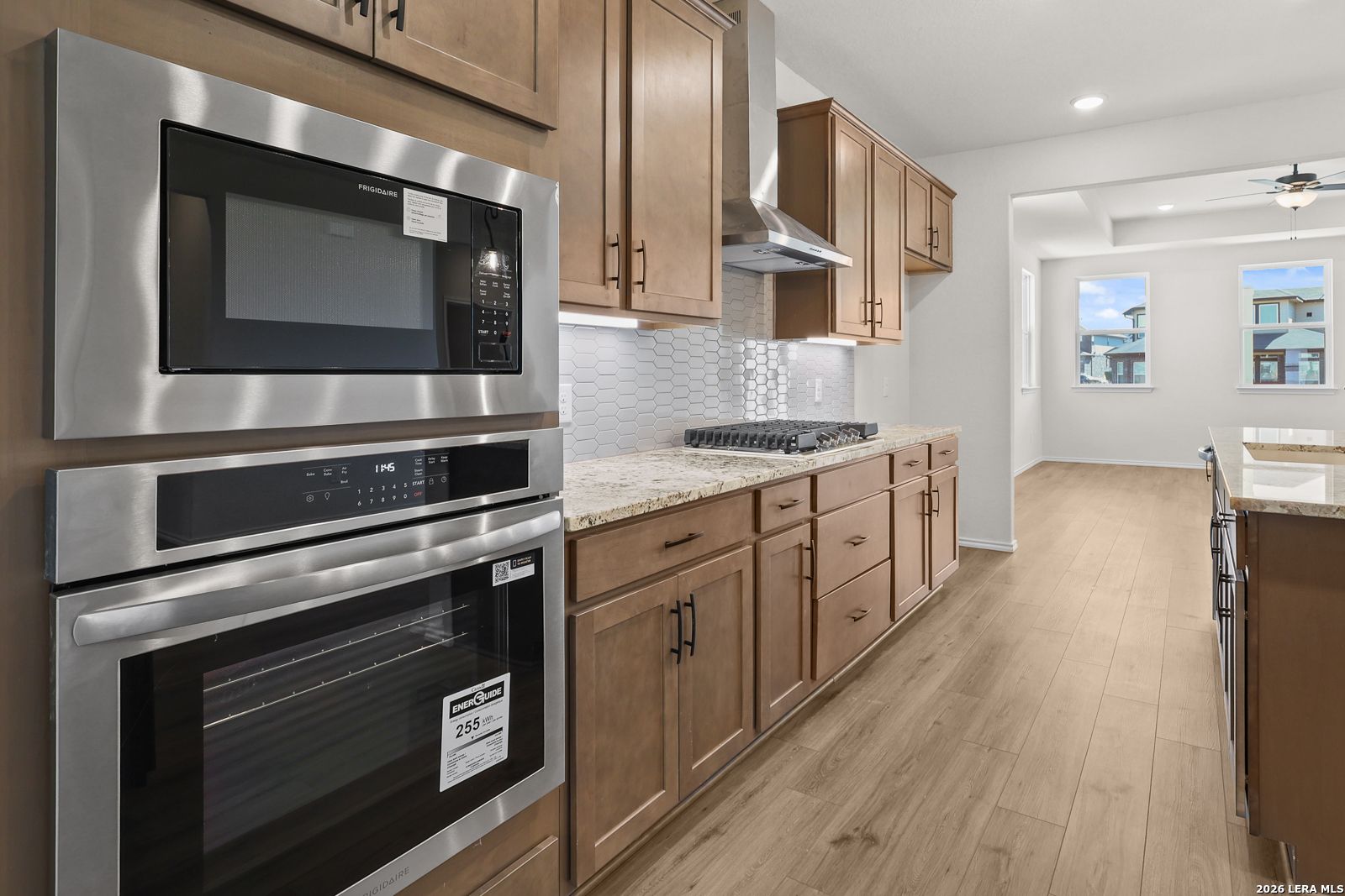 Modern kitchen with stainless wall oven, microwave, gas cooktop, and wood cabinets in Davidson Homes Glenwood E, San Antonio