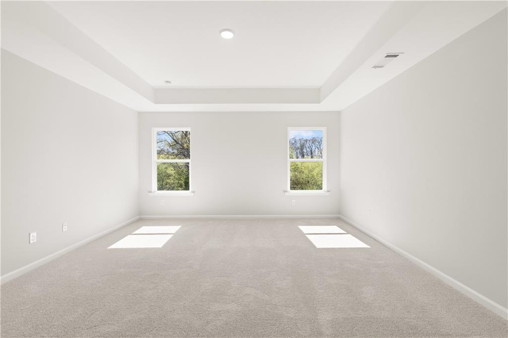 Bright empty bedroom with tray ceiling, light gray carpet, and large windows to greenery in The Hickory B, Winder, Georgia