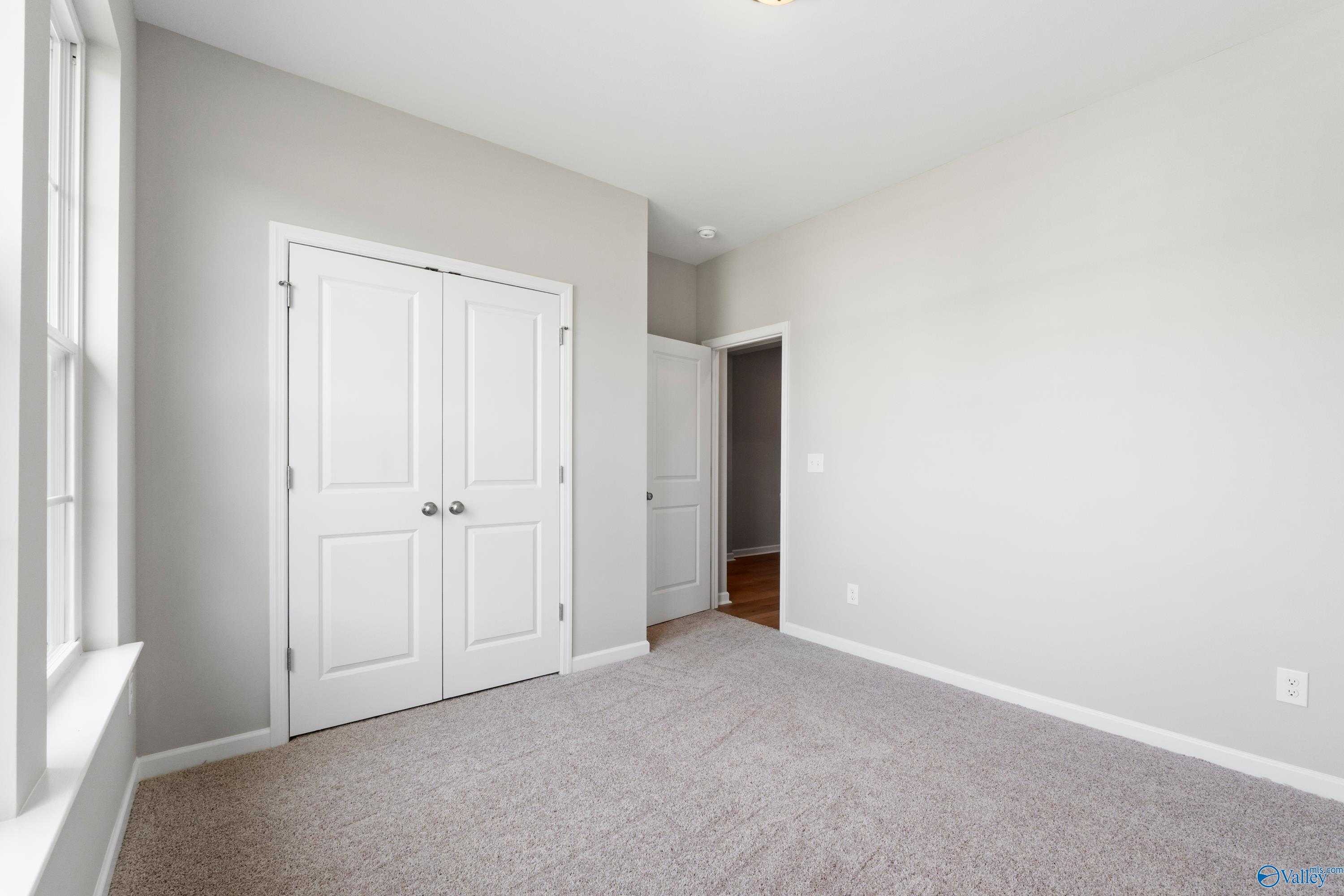 Spacious empty bedroom with light gray walls, white double closet doors, and large window in The Aurora floor plan, Harvest, Alabama