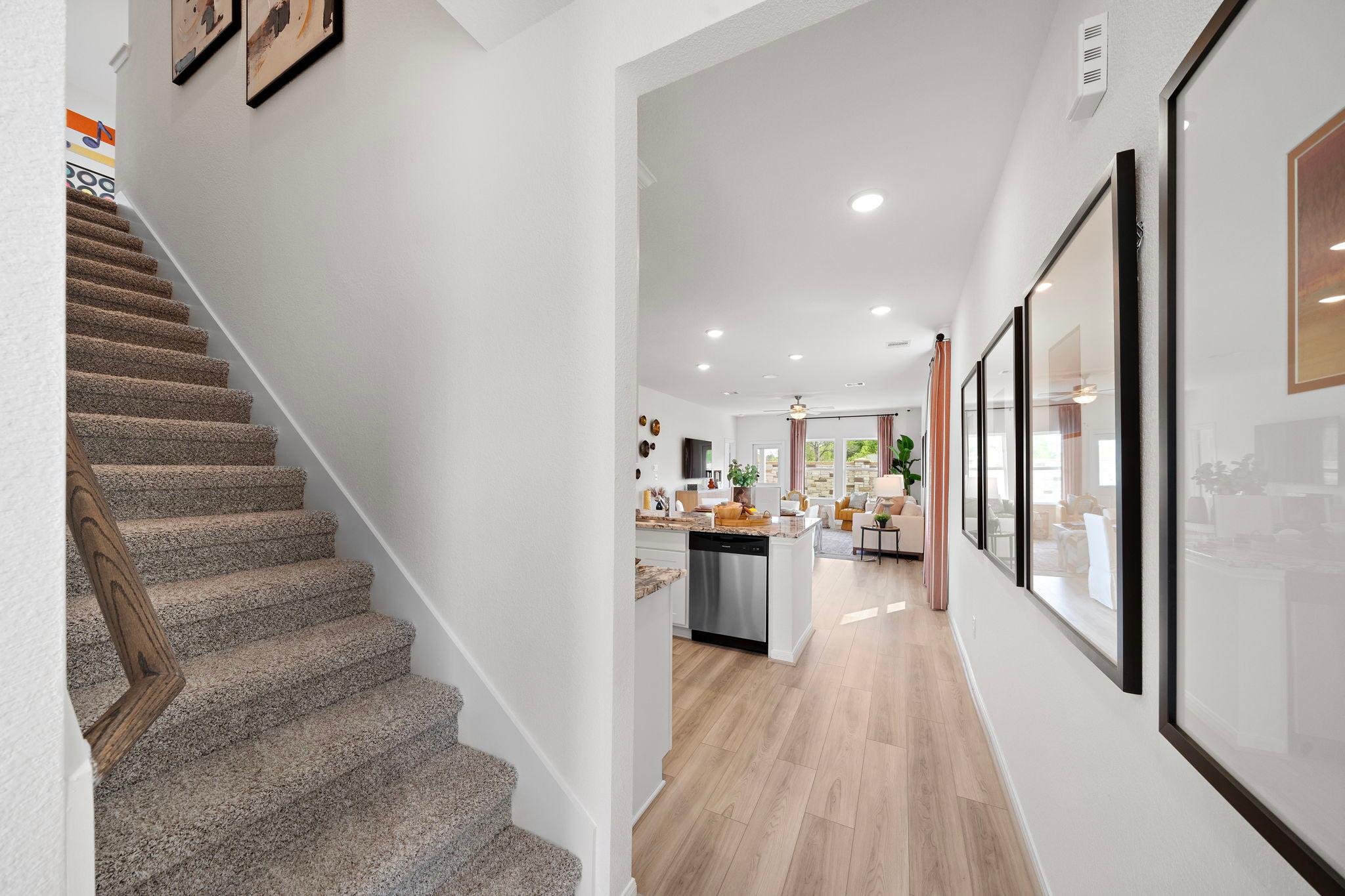 Spacious open hallway and kitchen interior at The Villages at WestPointe in Dayton Texas with carpeted staircase light wood floors and white cabinetry