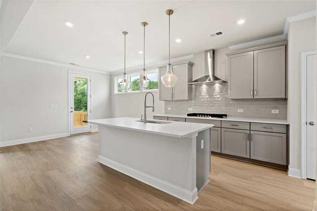 Modern kitchen with white quartz island, gray shaker cabinets, stainless hood, and French doors to backyard in The Willow B, Hoschton, GA