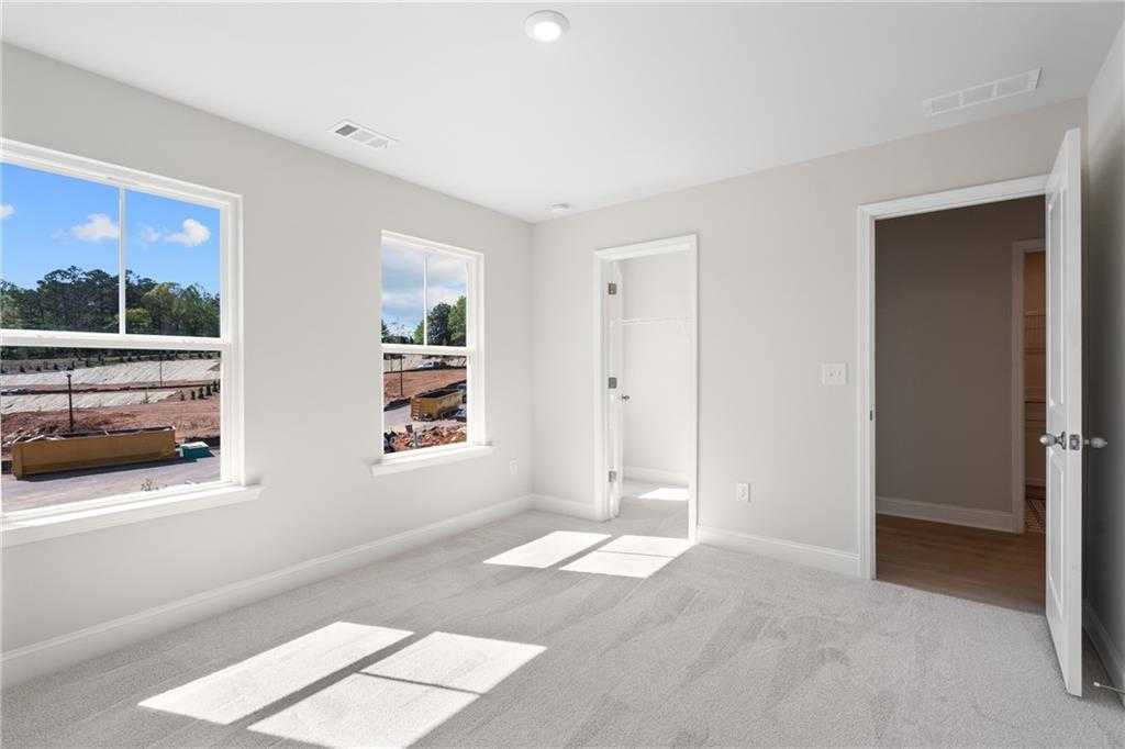 Bright secondary bedroom with gray walls, carpet floor, and large windows overlooking trees in The Hickory B, Buford, GA