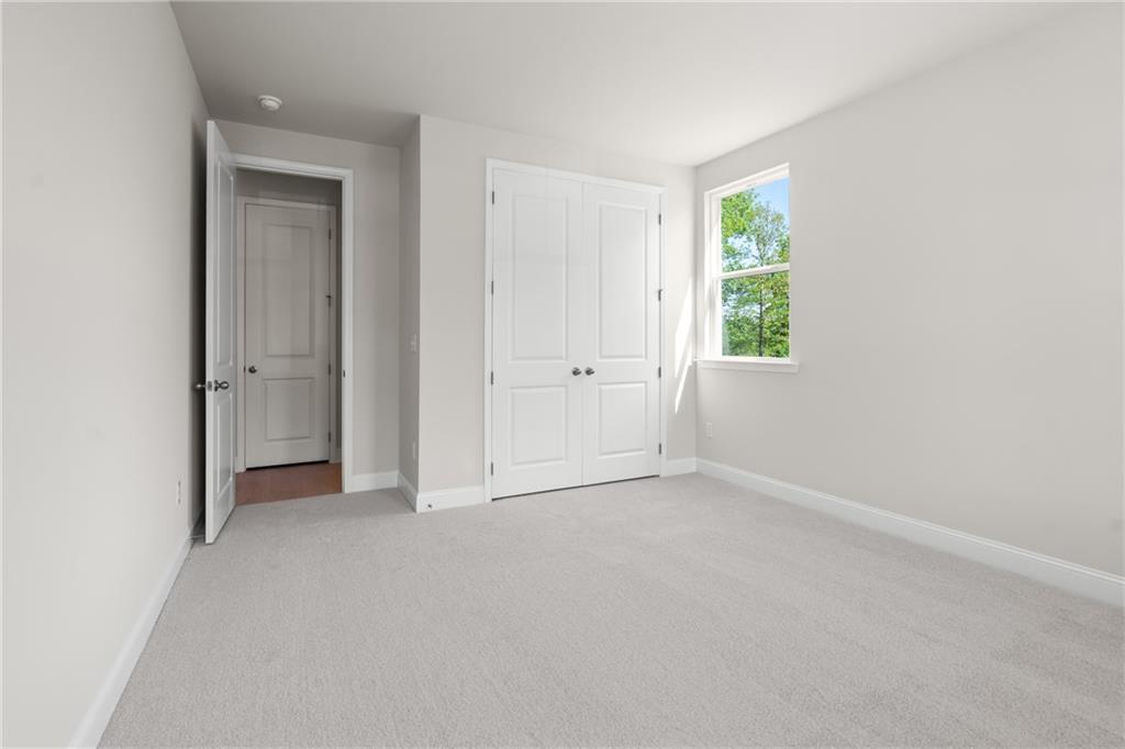 Spacious bedroom with gray carpet, light walls, double closet doors, en-suite bath access in The Hickory E, Buford, GA