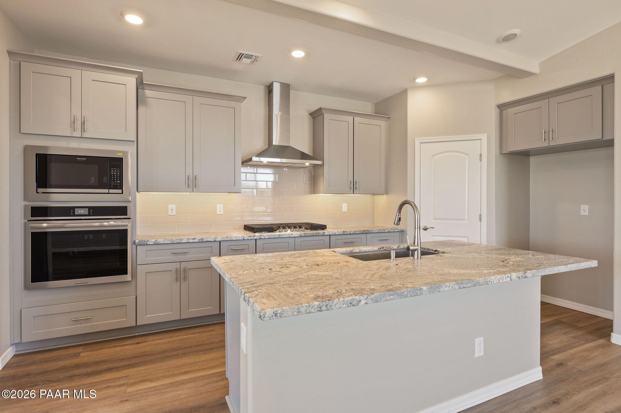 Modern kitchen with gray shaker cabinets, granite island sink, stainless double ovens and hood in Davidson Homes The Frontier A, Prescott Valley AZ