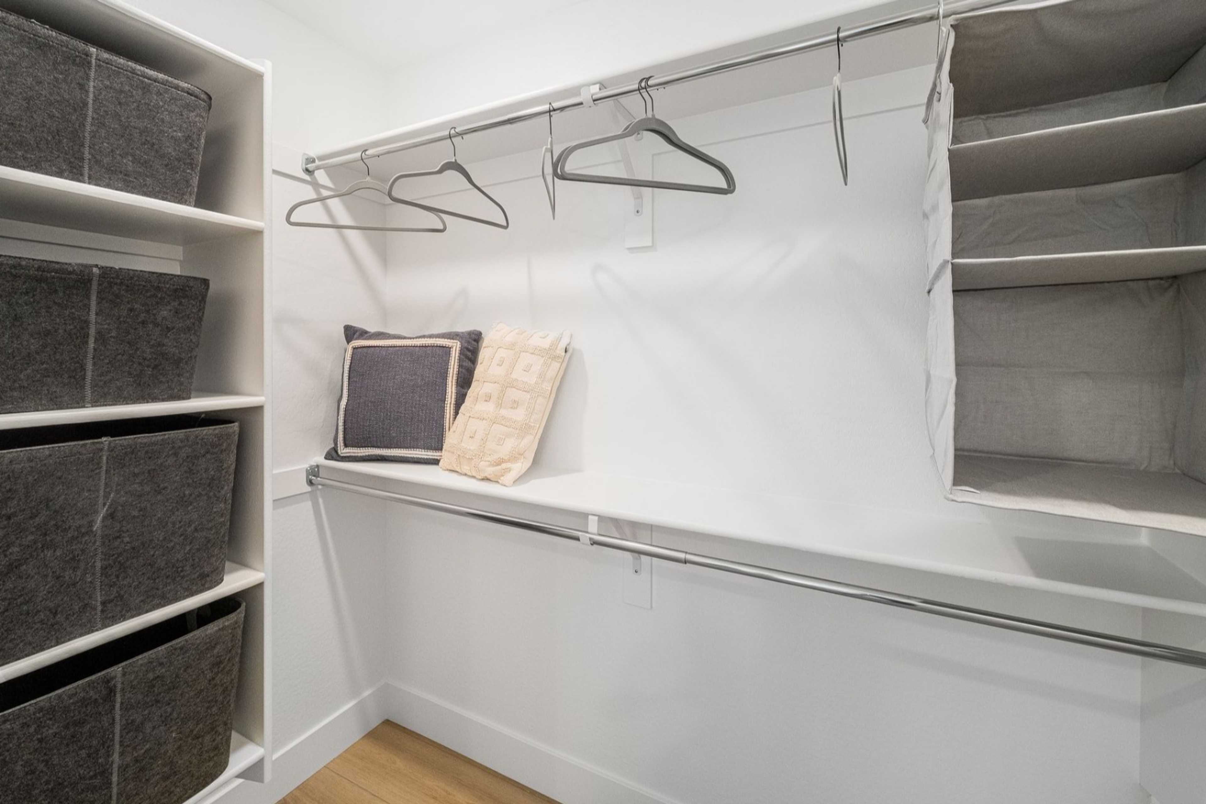 Spacious master walk-in closet in The Wilmington home featuring white shelving, gray fabric bins, and hanging rods