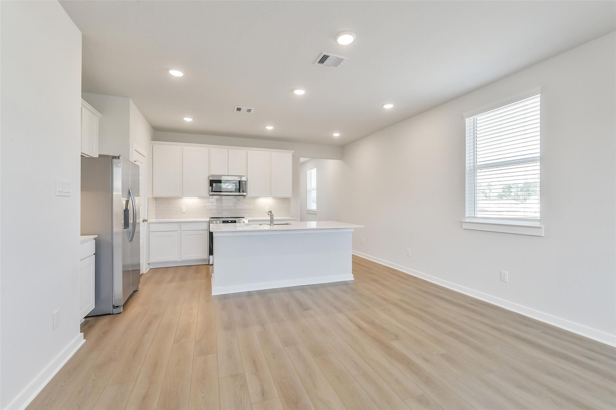 Modern white kitchen with island, stainless steel appliances, and hardwood floors in Davidson Homes The Colorado F, Cleveland, TX