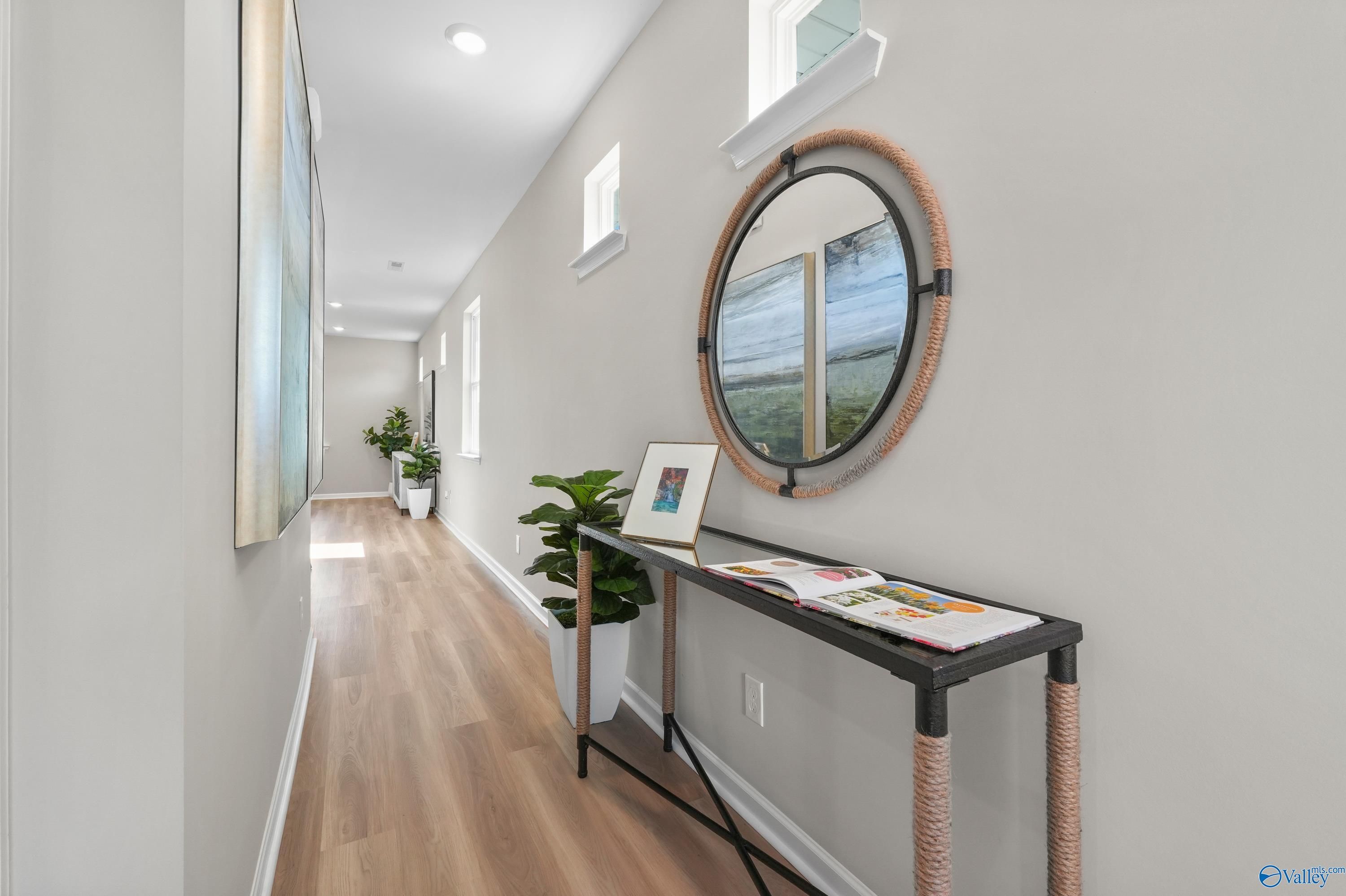 Elegant hallway with light oak floors, rattan mirror, console table, and plants in The Malibu 2-bedroom home, Evergreen Mill, Madison, Alabama