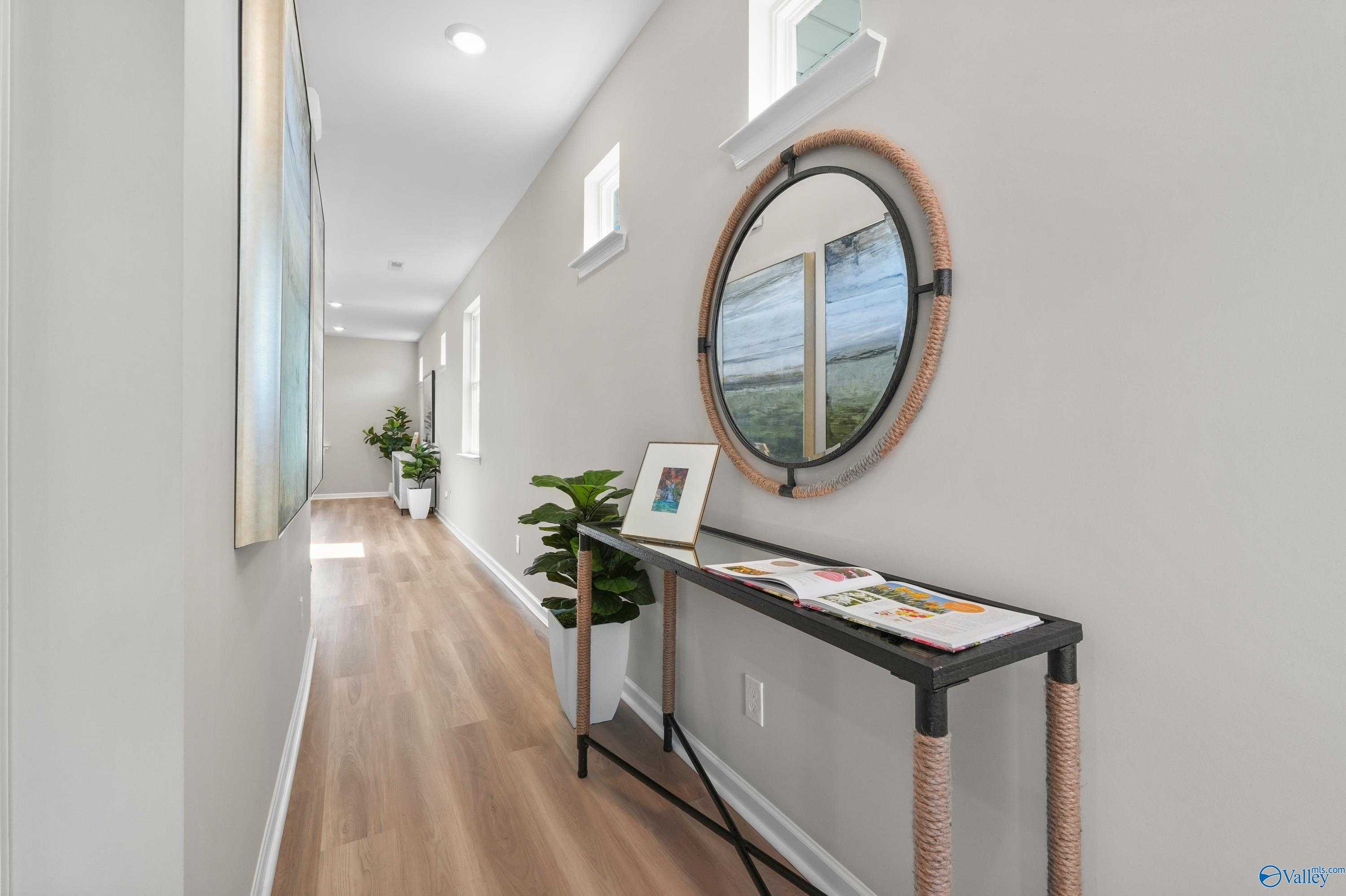 Elegant hallway with light oak floors, rattan mirror, console table, and plants in The Malibu 2-bedroom home, Evergreen Mill, Madison, Alabama