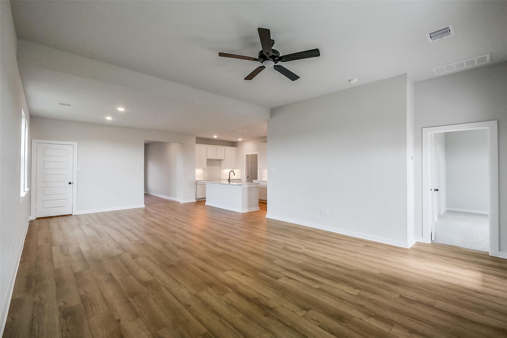 Open-concept living room with hardwood floors, white kitchen island, and ceiling fan in Davidson Homes The Tierra B, Beasley, Texas