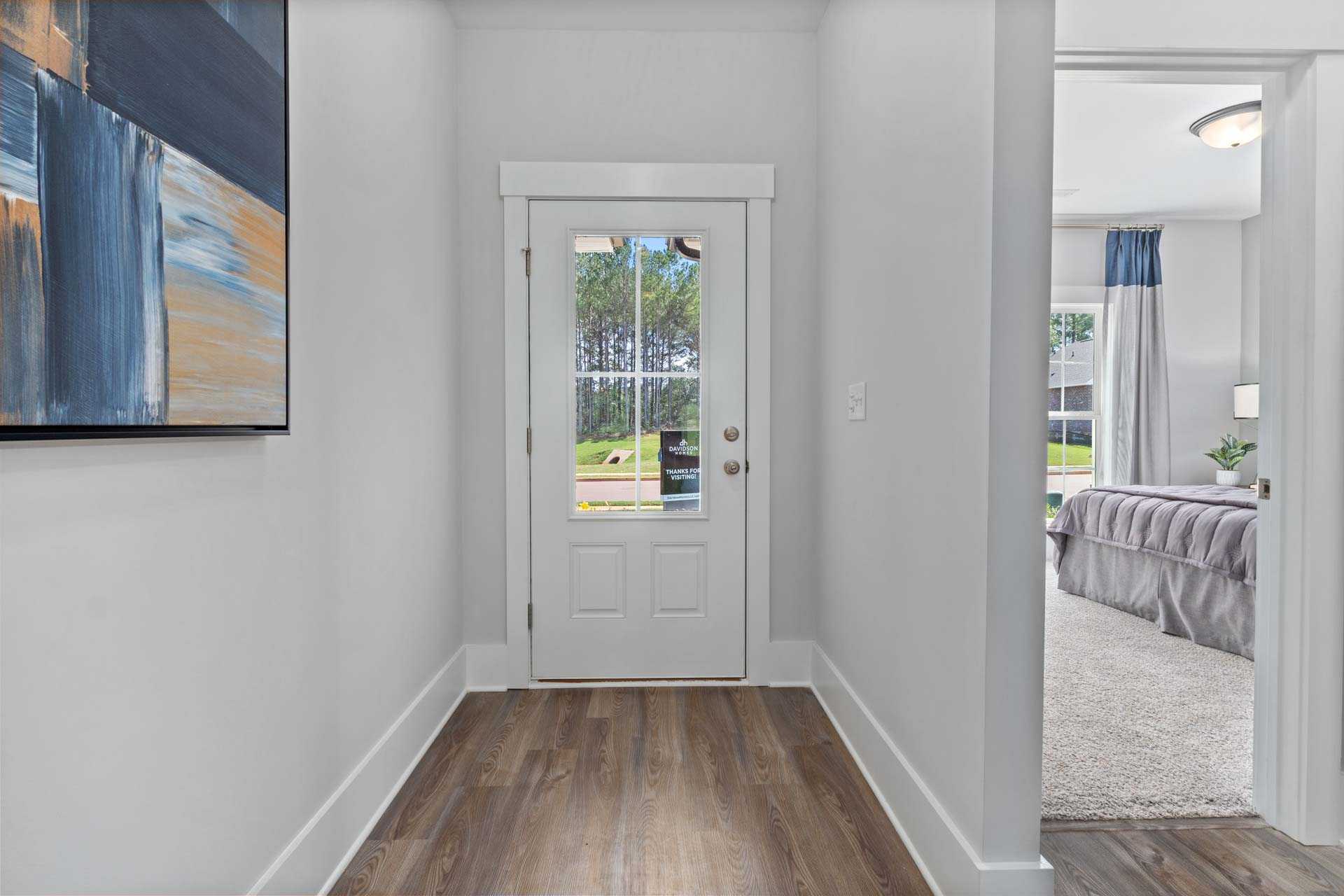 Spacious hallway with glass backyard door at Blue Spring in Huntsville AL by Davidson Homes, hardwood floors, abstract art, bedroom view