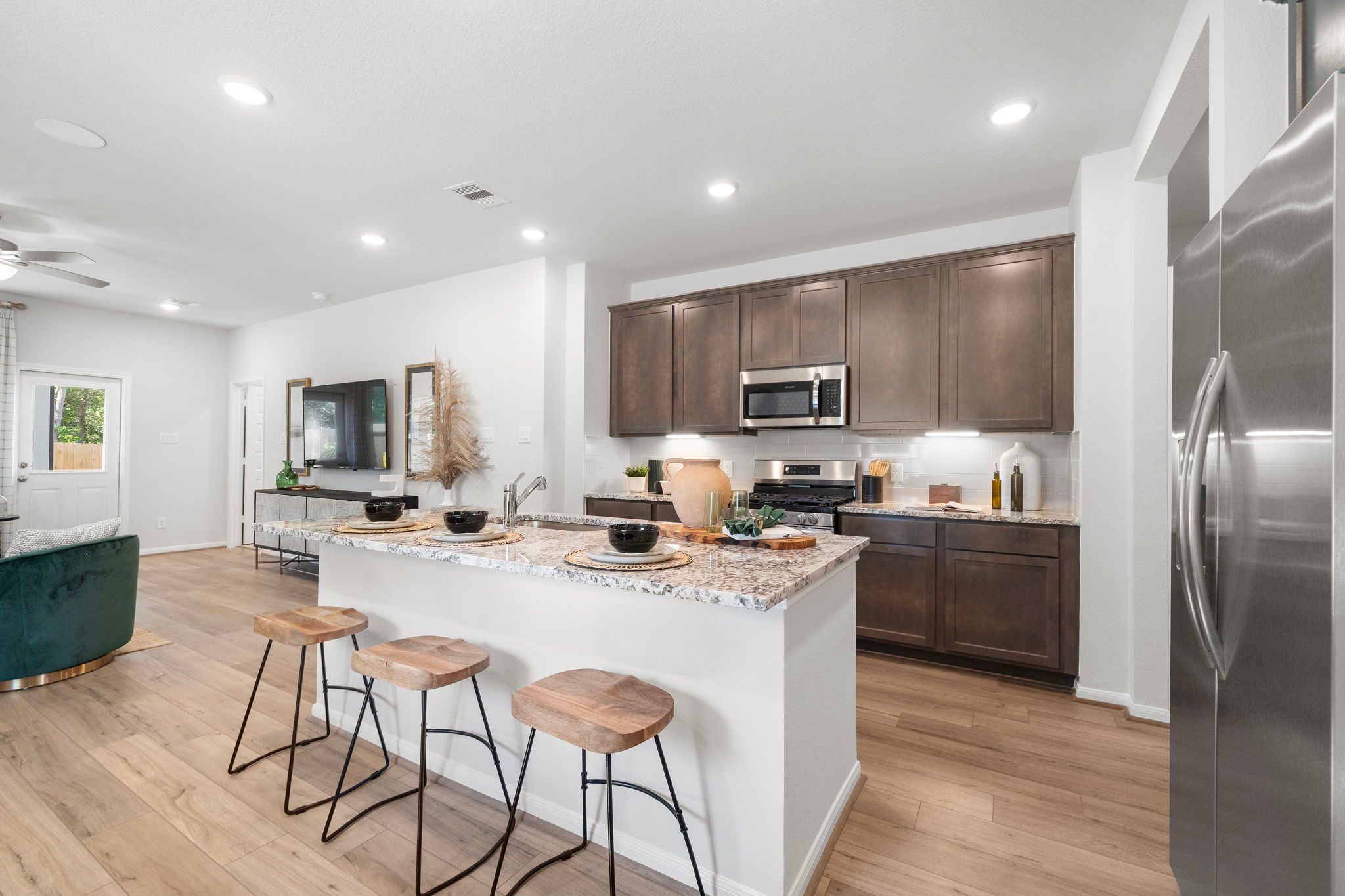 Open-concept kitchen at Robins Landing in Houston TX with granite island, wooden stools, dark cabinets, stainless appliances, hardwood floors
