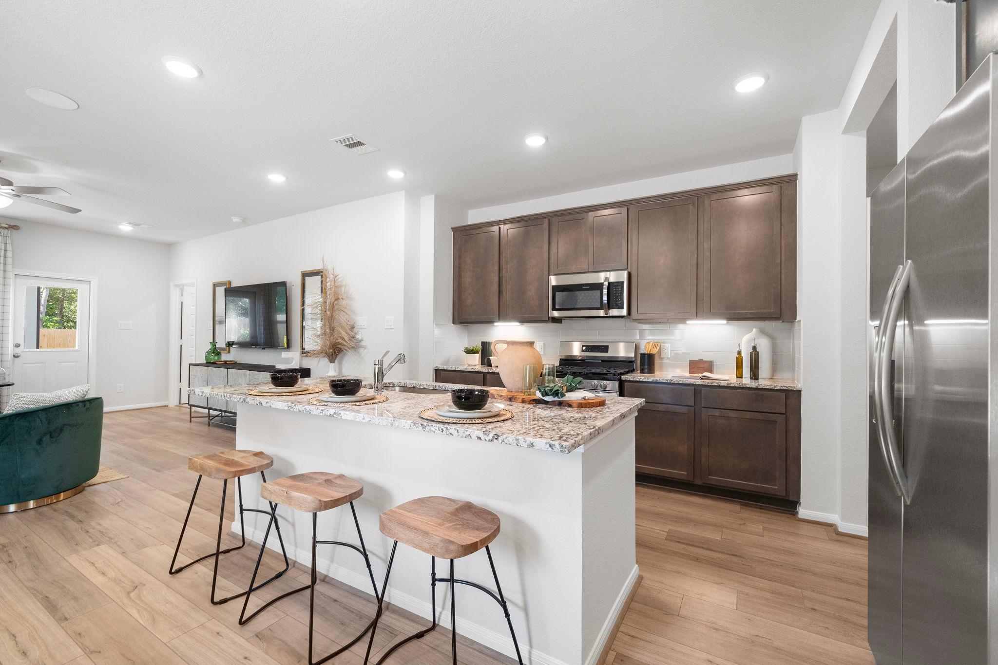 Open-concept kitchen at Robins Landing in Houston TX with granite island, wooden stools, dark cabinets, stainless appliances, hardwood floors
