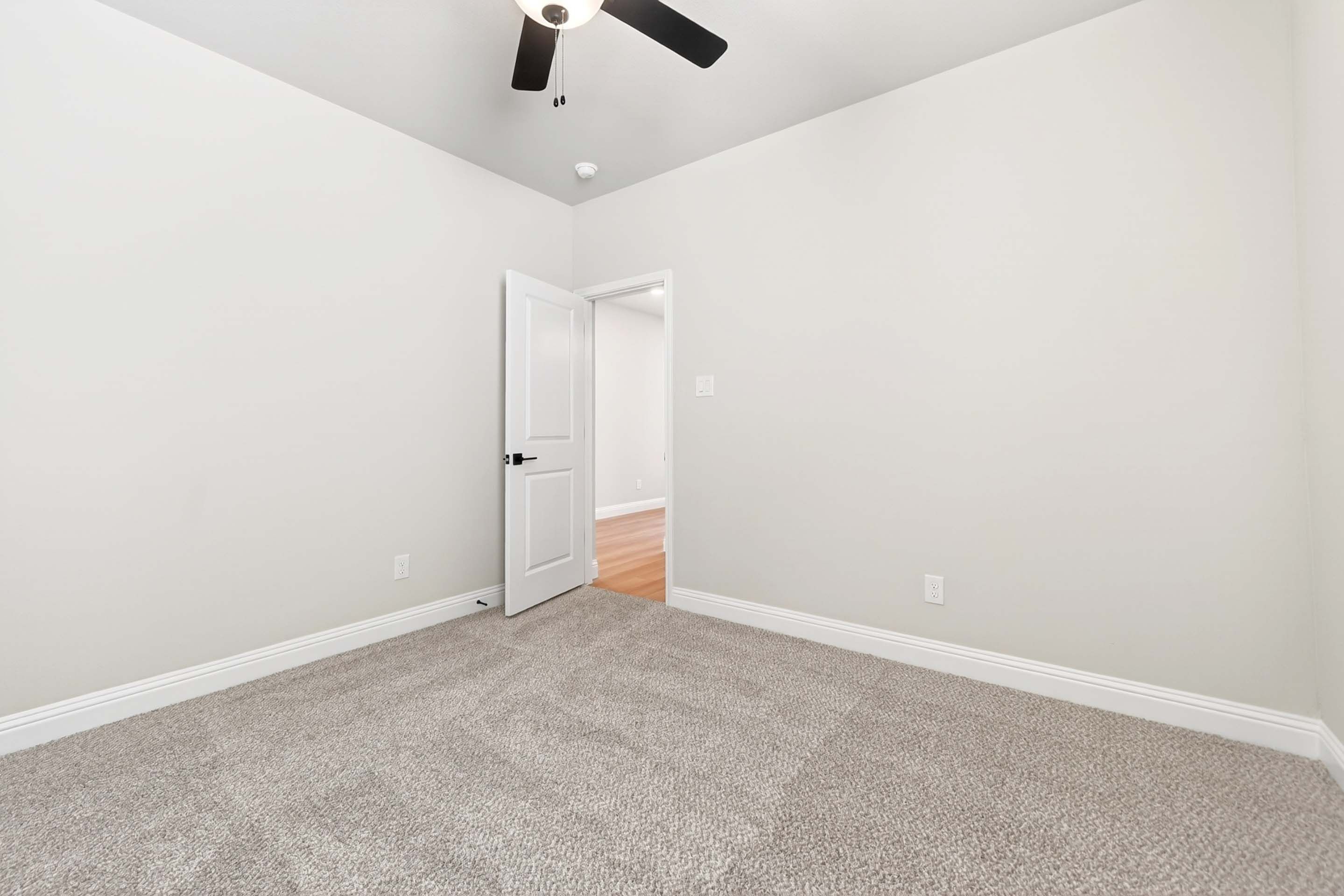 Spacious secondary bedroom in The Holly with plush carpeting, neutral walls, and a ceiling fan in Royse City, Texas.