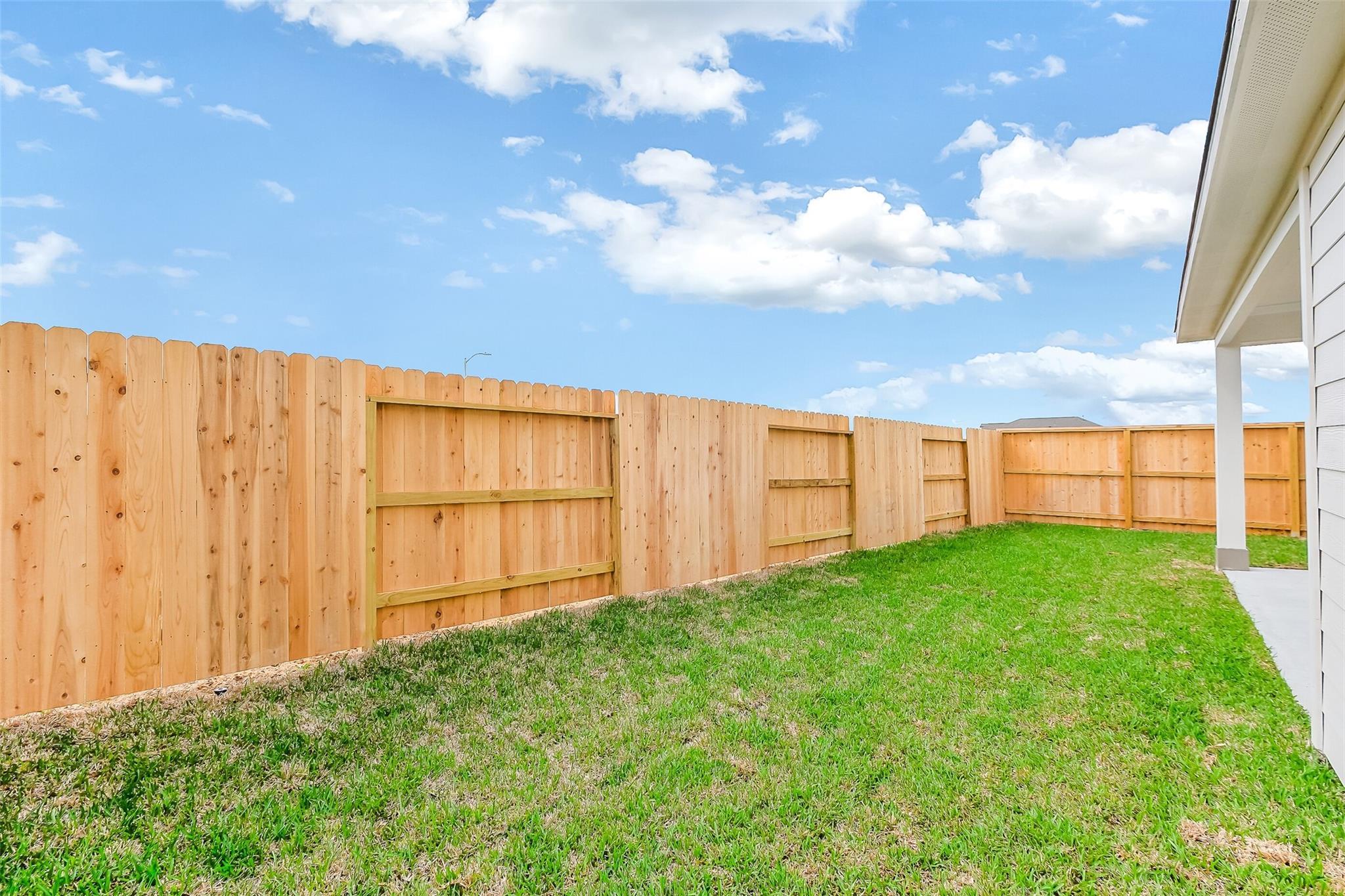 Private backyard with cedar privacy fence and lush green lawn beside white home in Emberly, Beasley, Texas