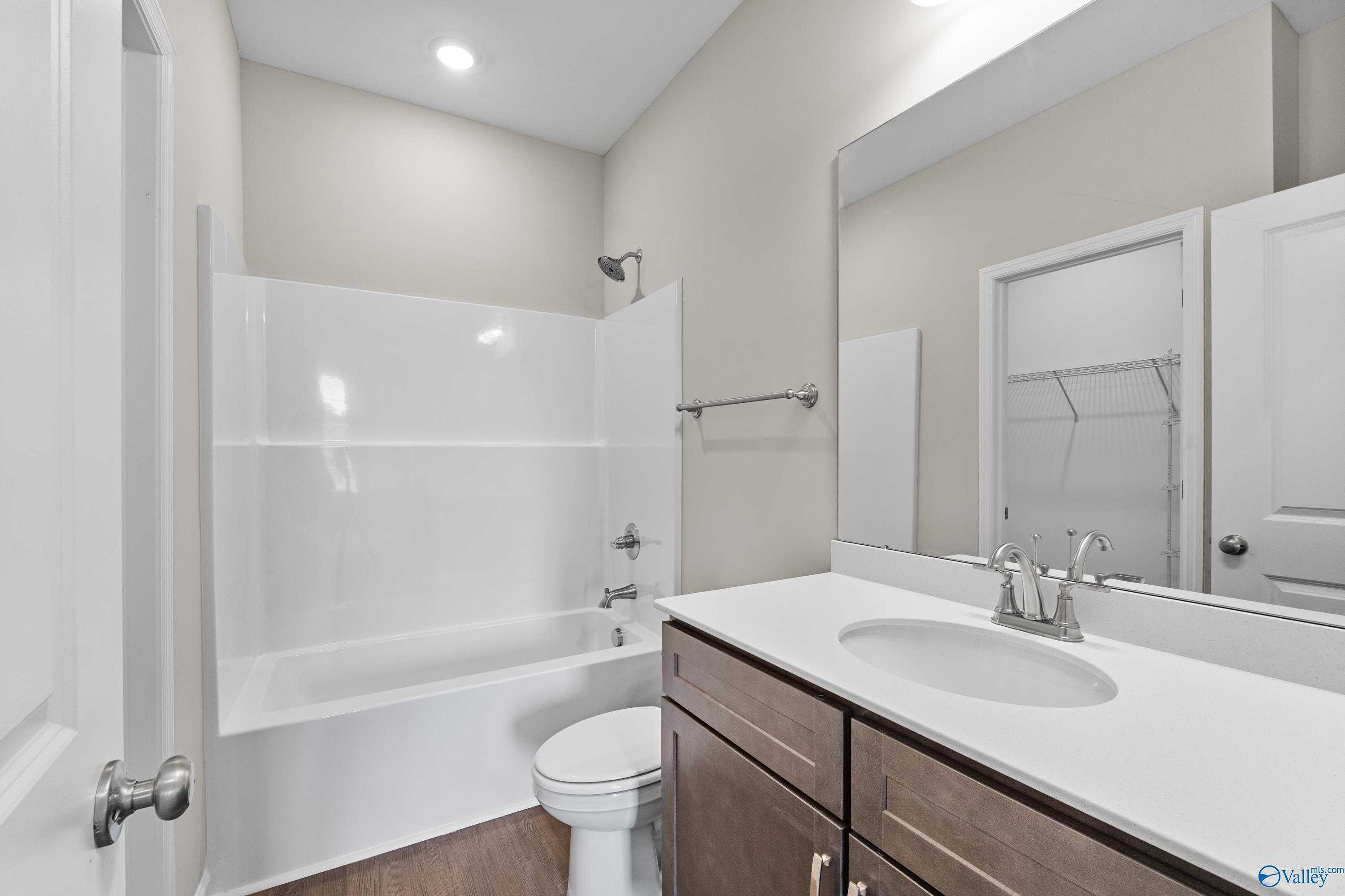 Modern guest bathroom with white tub-shower combo, single vanity, and linen closet in Davidson Homes The Sanctuary, Huntsville, Alabama