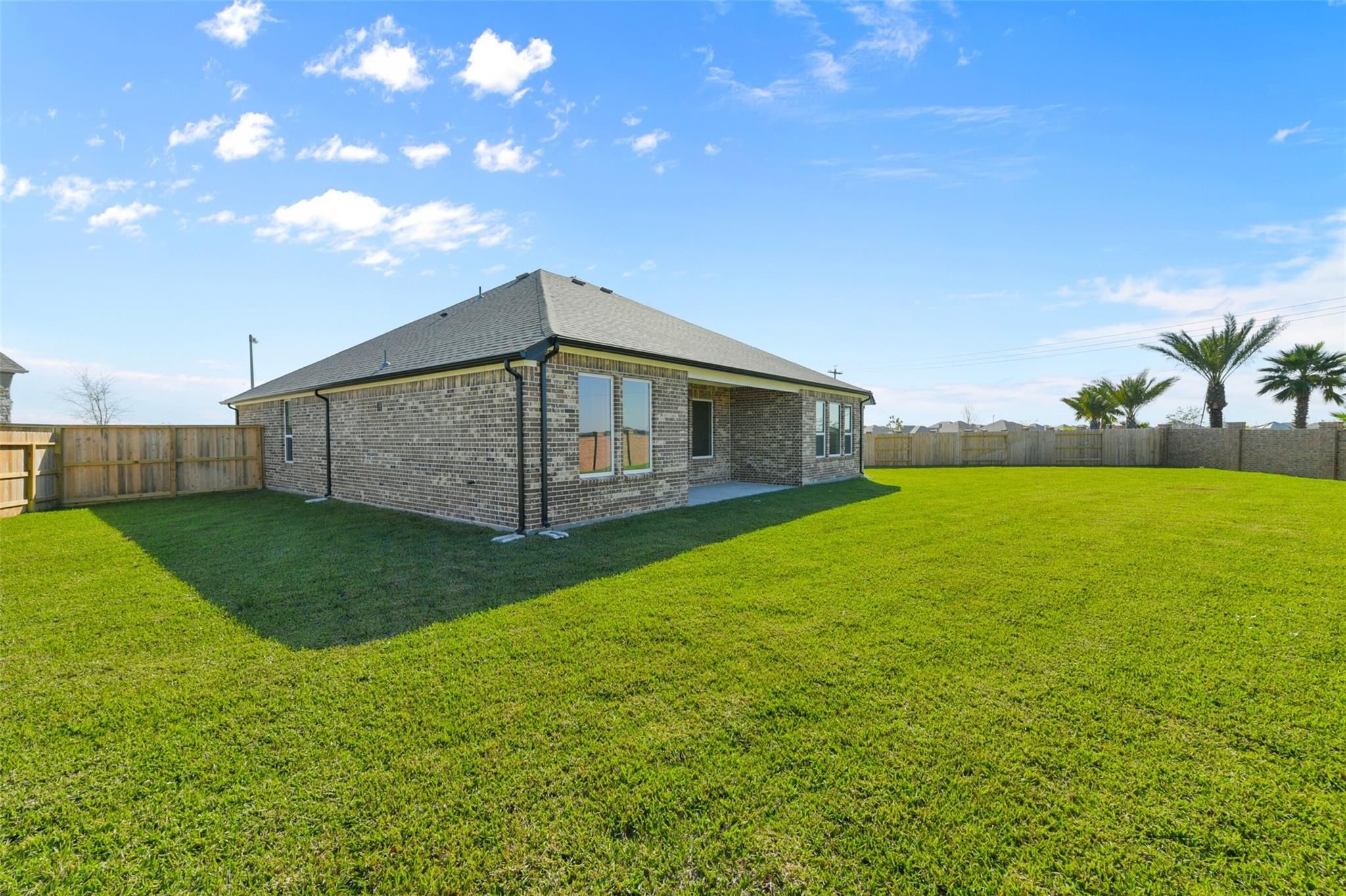 Single-story brick home with 2-car garage, lush green yard, wooden fence and palm trees in Lago Mar, Texas City, Texas - Davidson Homes Edward C