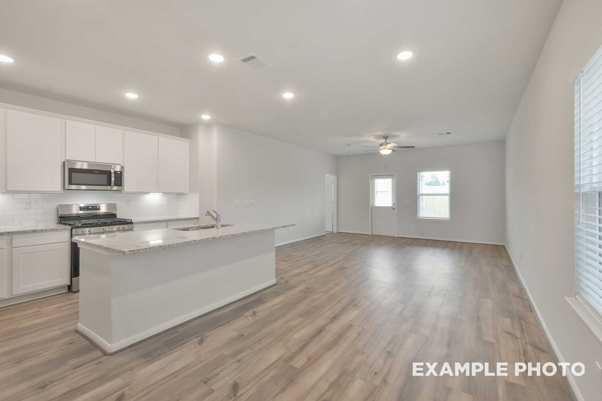 Open-concept kitchen and living area in The Brazos by Davidson Homes, featuring white cabinetry, granite island, and LVP flooring
