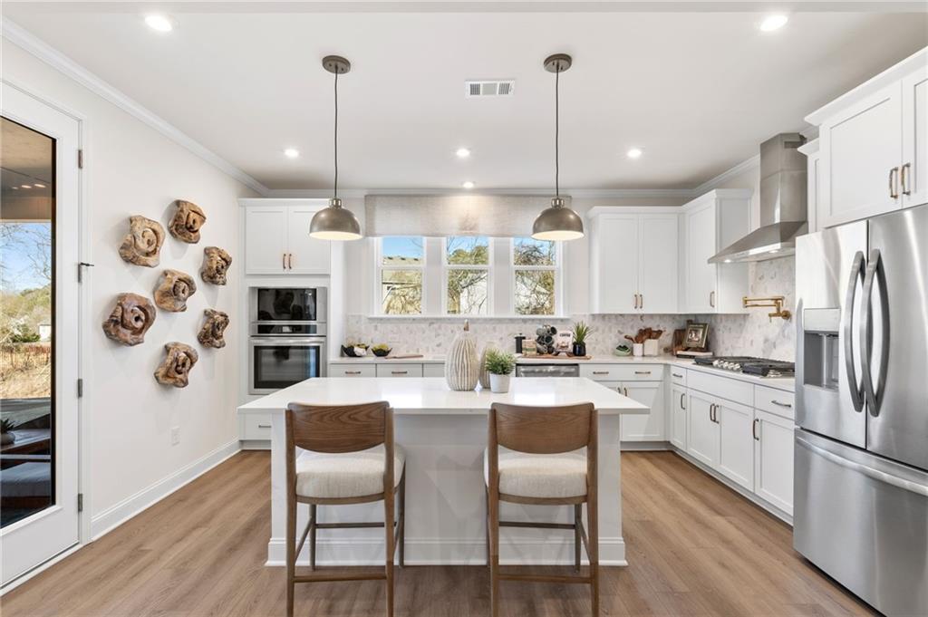 Modern white kitchen with island, stainless appliances, and pendant lighting in The Aspen C home at Fern Hollow, Buford.