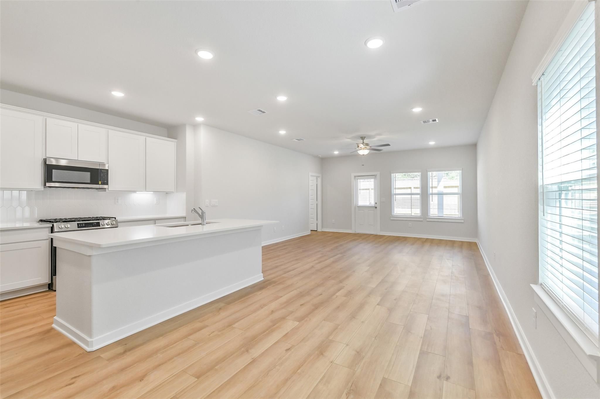 Modern open-concept kitchen with white cabinets, stainless steel appliances, island bar, and hardwood floors in Davidson Homes Blanco E, Magnolia, Texas
