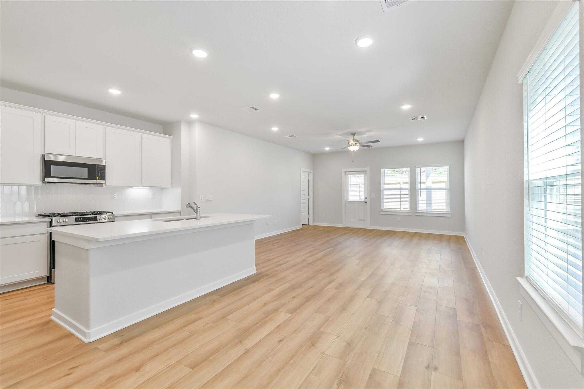 Modern open-concept kitchen with white cabinets, stainless steel appliances, island bar, and hardwood floors in Davidson Homes Blanco E, Magnolia, Texas