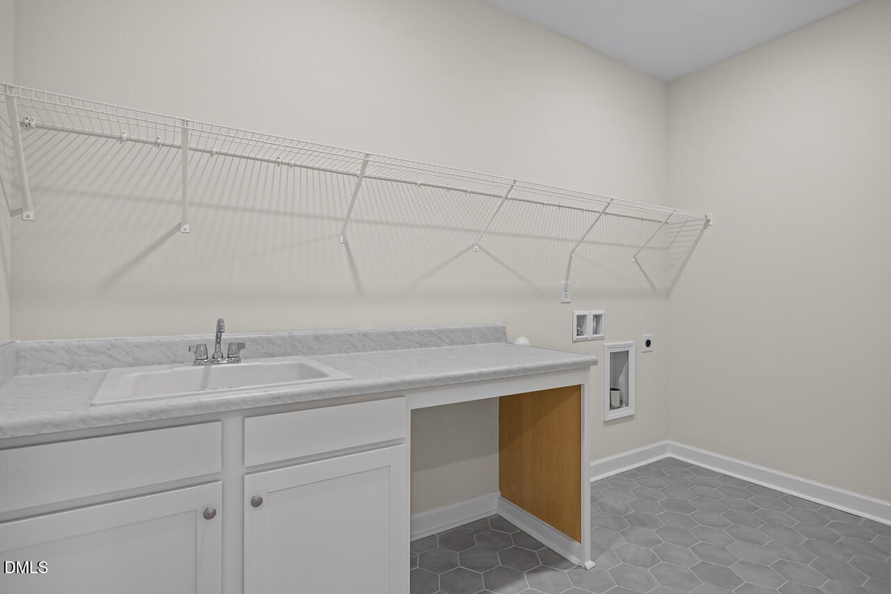 Laundry room with utility sink, white cabinets, and wire shelving in The Hickory II B home by Davidson Homes in Montrose.