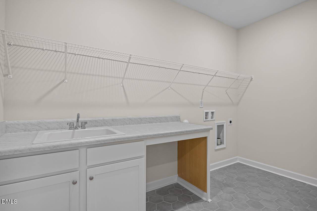 Laundry room with utility sink, white cabinets, and wire shelving in The Hickory II B home by Davidson Homes in Montrose.