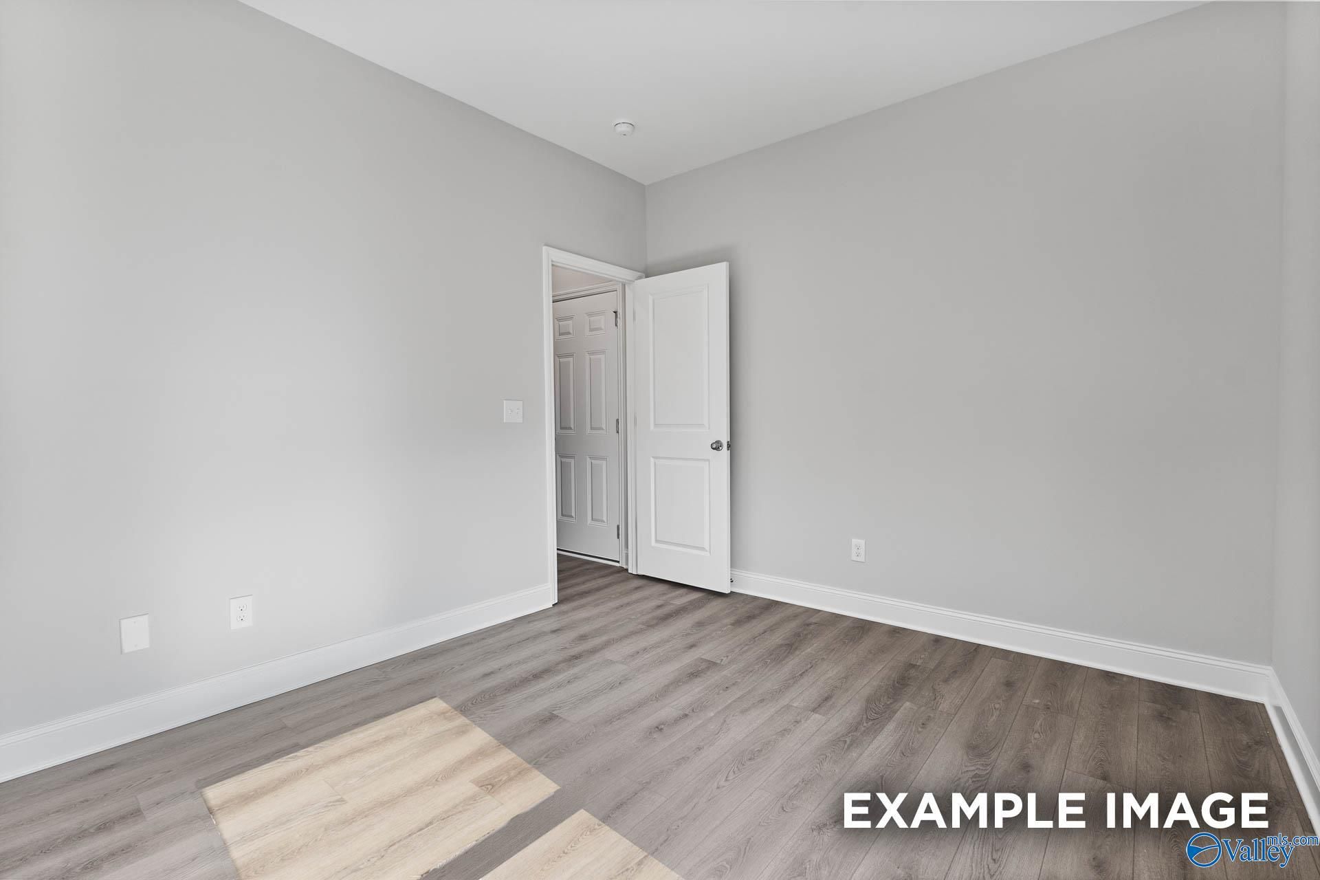 Bright bedroom with light gray walls, hardwood floors, and open door to ensuite in Davidson Homes The Daphne C, Arab, Alabama