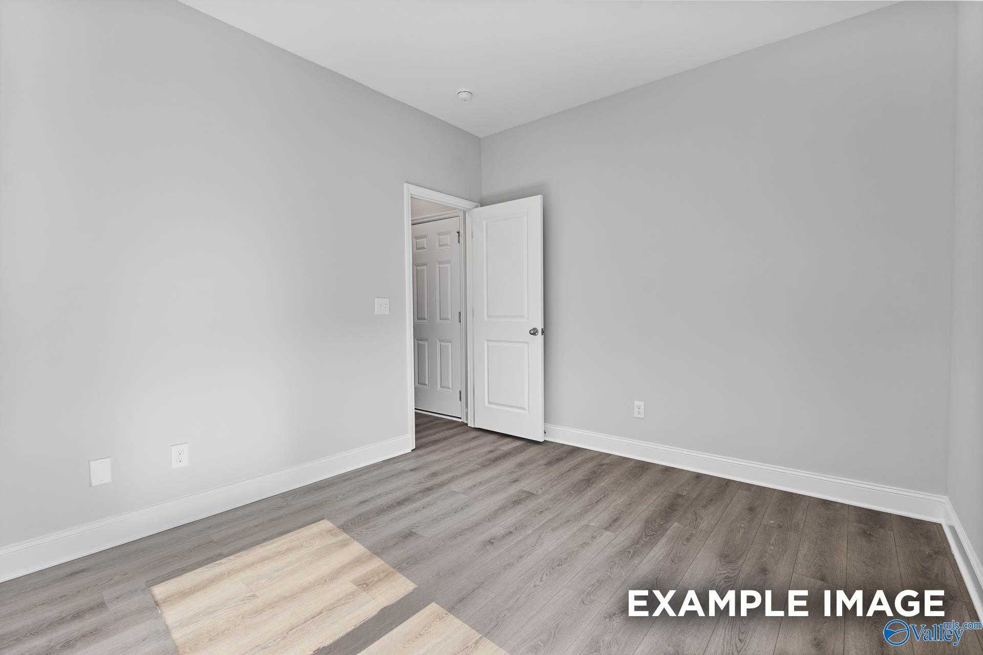 Bright bedroom with light gray walls, hardwood floors, and open door to ensuite in Davidson Homes The Daphne C, Arab, Alabama