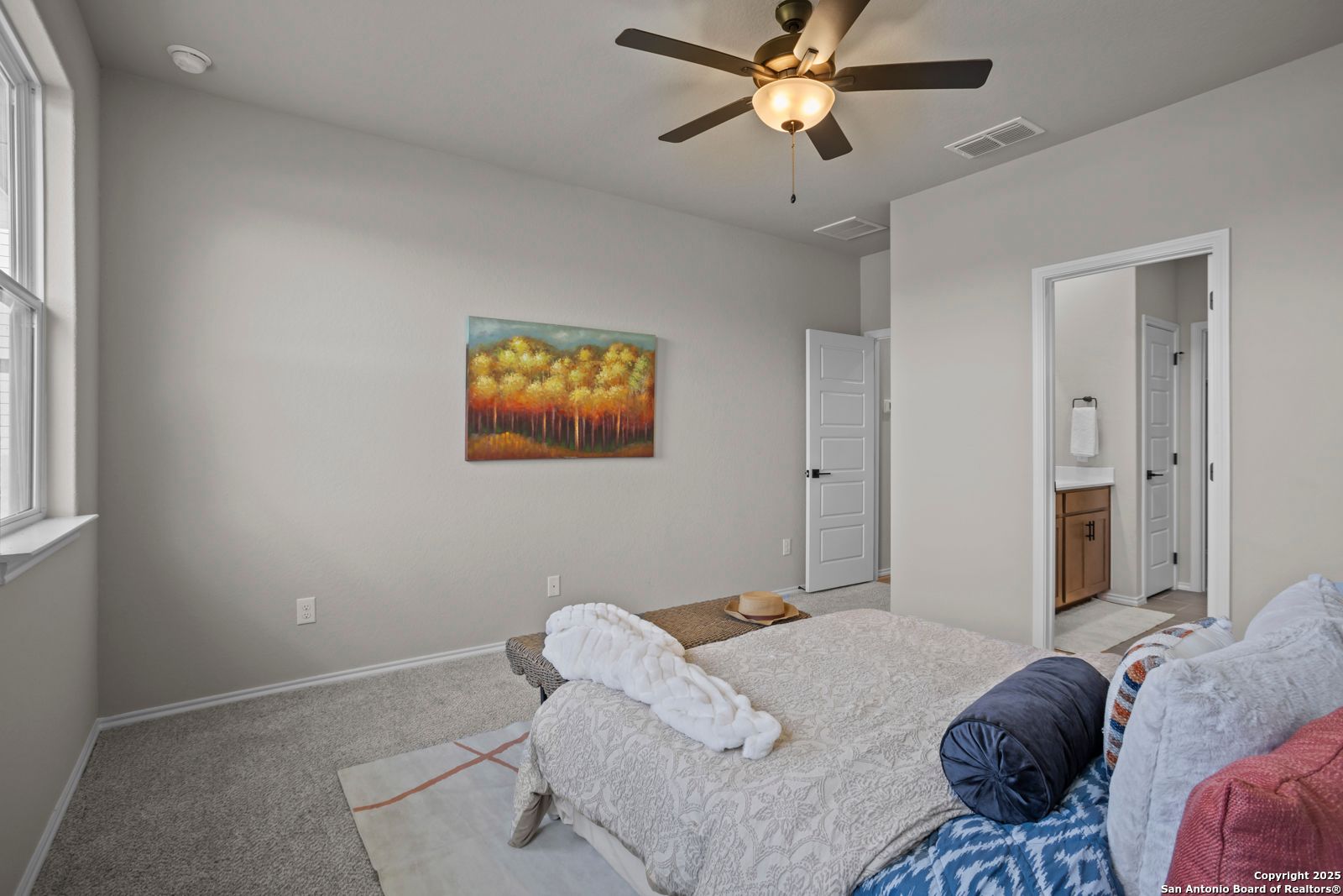 Master bedroom with king bed, gray walls, ceiling fan, abstract tree painting, and en-suite bath in The Asheville H, Converse, Texas