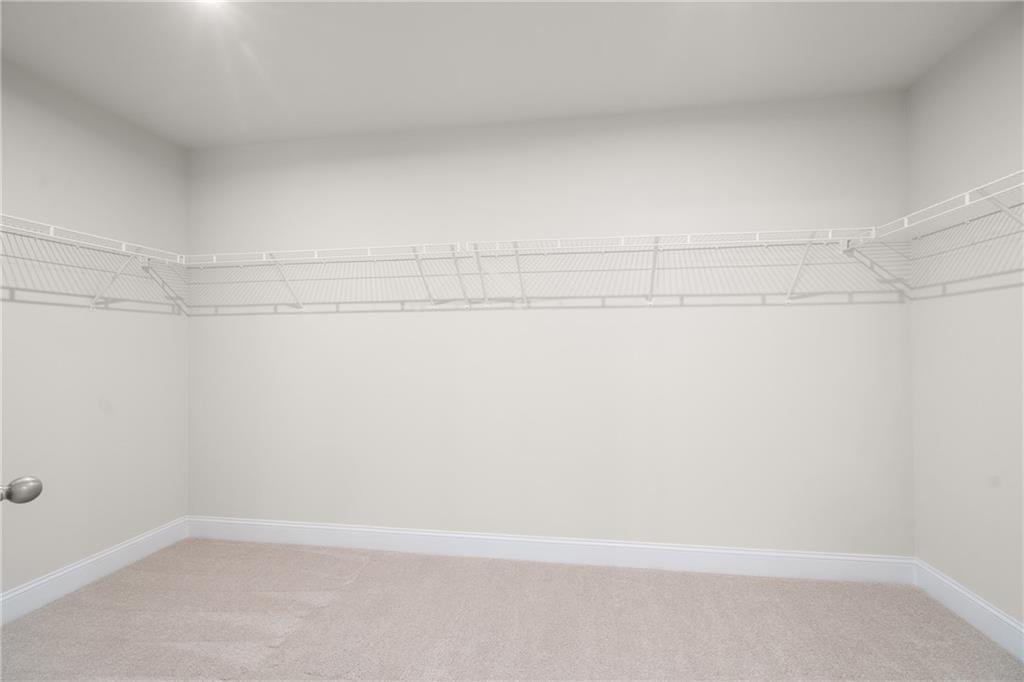 Empty walk-in closet with white wire shelving, beige carpet, and neutral walls in Davidson Homes The Hickory E, Buford, Georgia