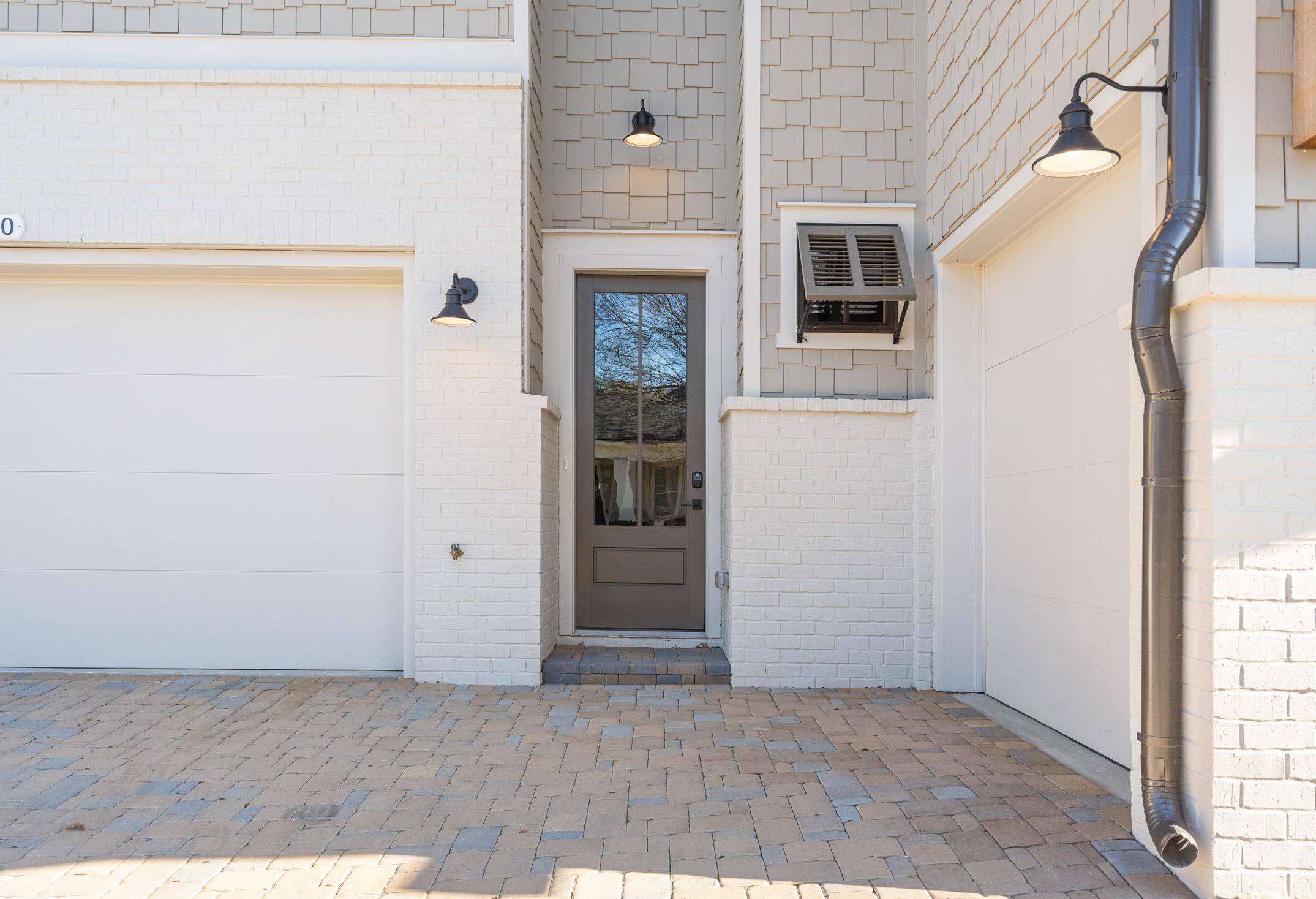 The Seaside 3-car garage facade with white siding, gray entry door, wall lanterns, shutters, and paver driveway in Woodstock, Georgia