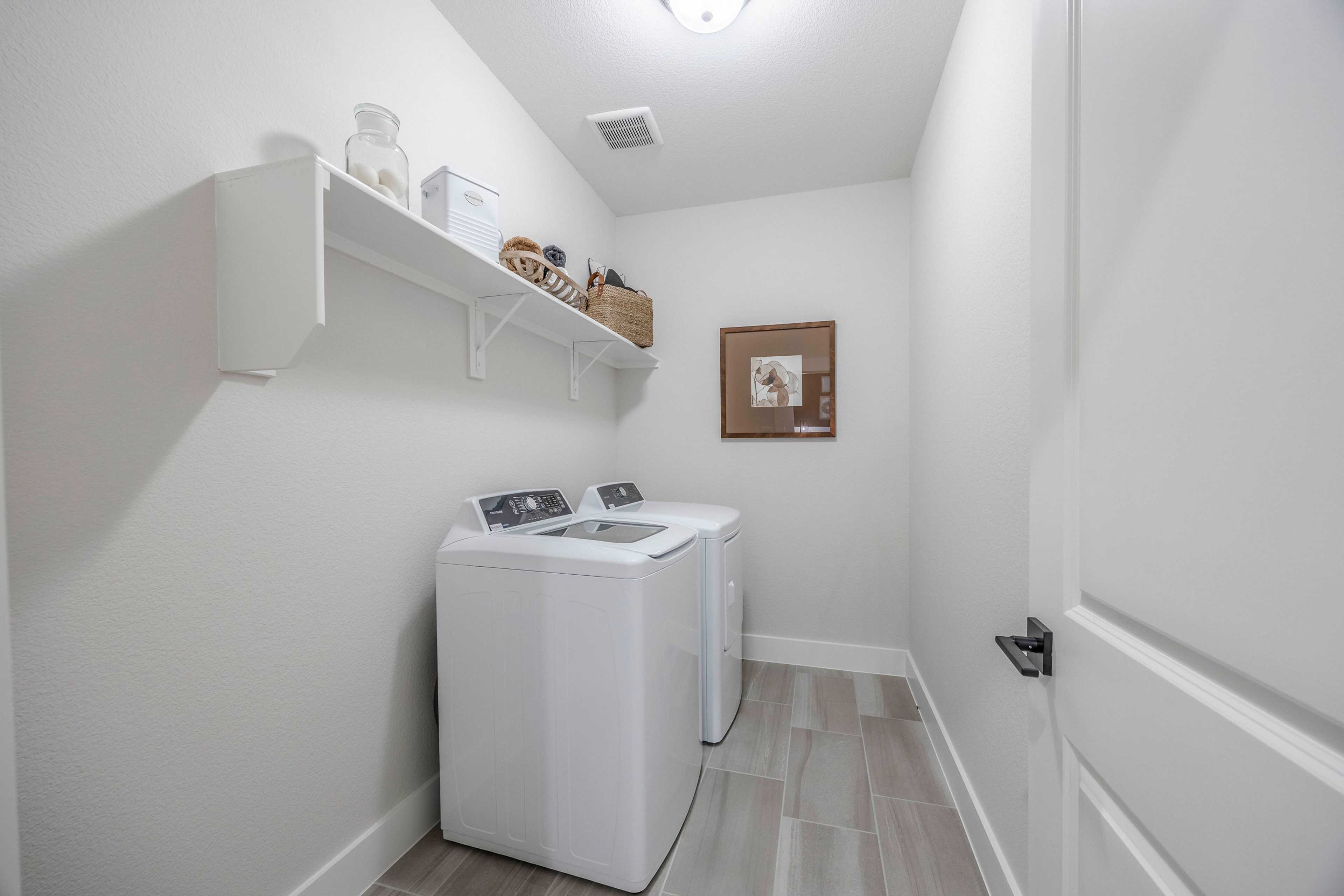 Spacious laundry room at Waverly Estates in Josephine Texas featuring side-by-side white washers, built-in shelves with woven baskets and glass jars