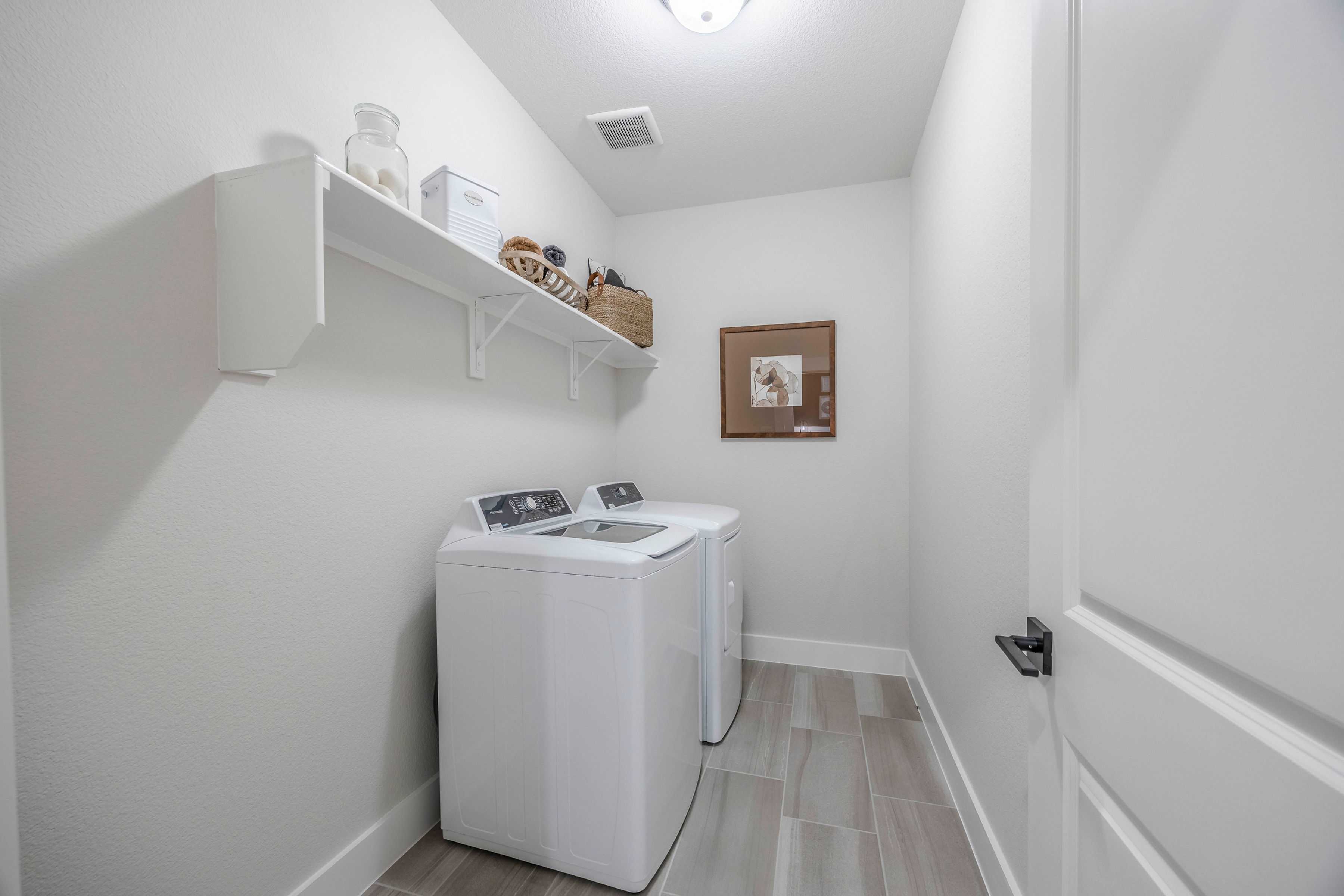 Spacious laundry room in The Rockford home with white washer dryer, built-in shelves, baskets and neutral tones