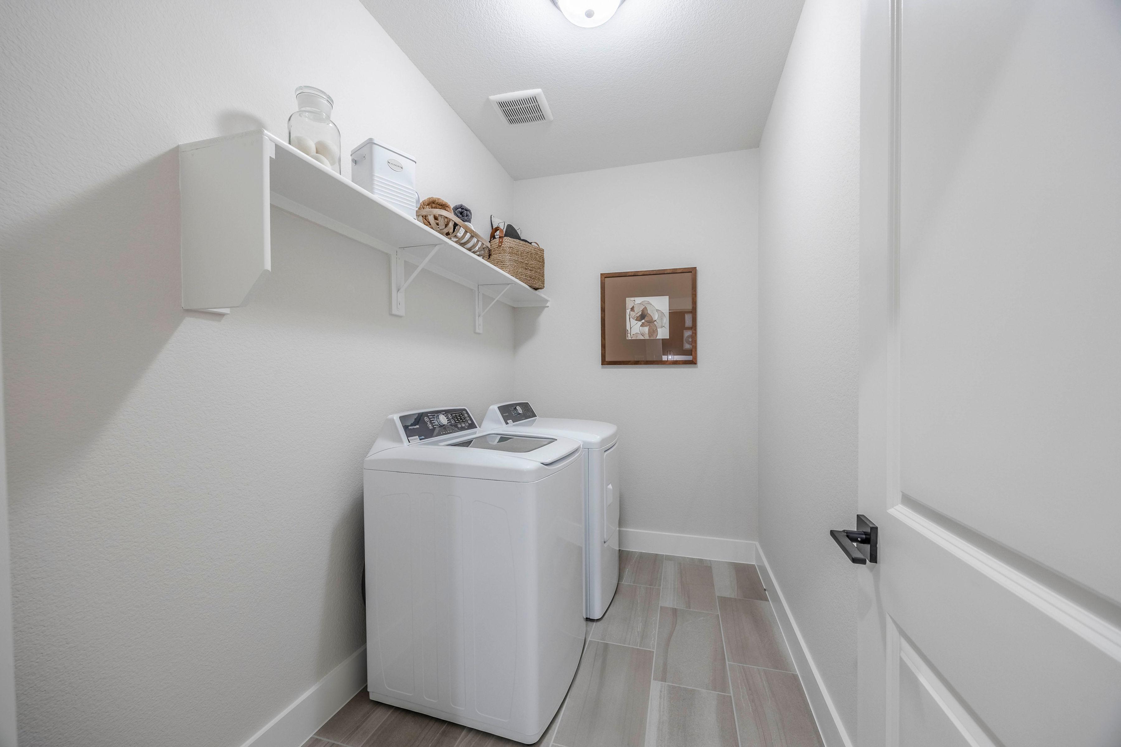 Spacious laundry room at Waverly Estates in Josephine Texas featuring side-by-side white washers, built-in shelves with woven baskets and glass jars