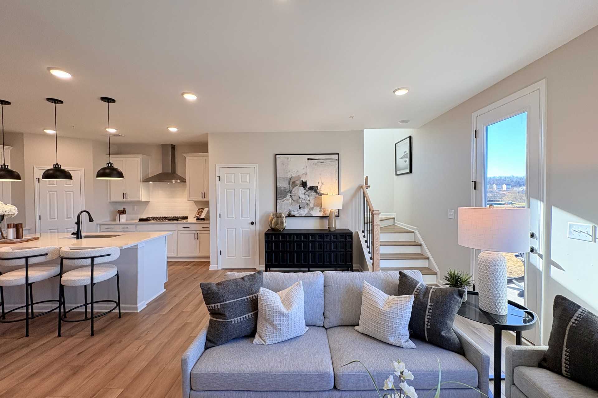 Open-concept living room and kitchen in Hemingway Cumming GA with gray sectional sofa, hardwood floors, white island, and pendant lights