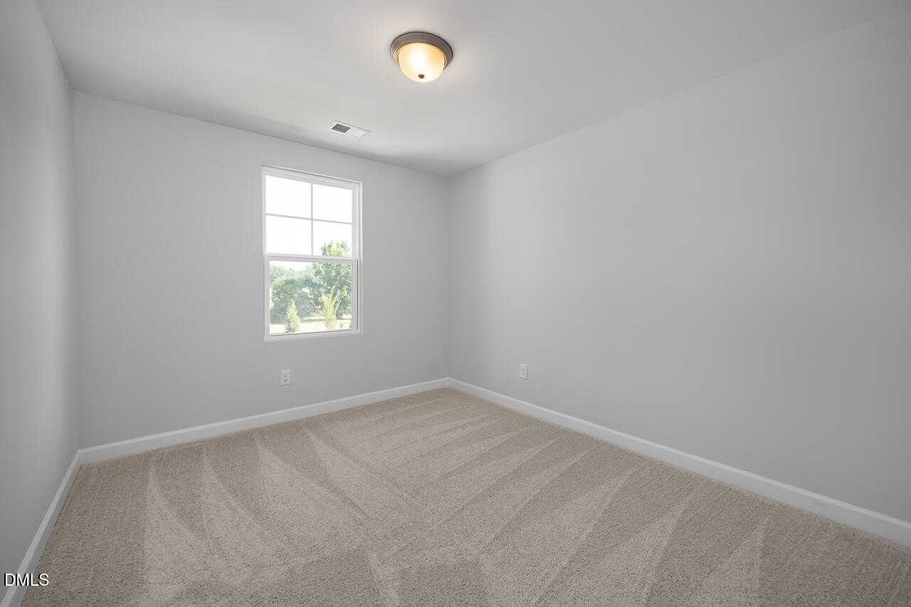Bright secondary bedroom with light gray walls, beige carpet, large window, and ceiling light in Davidson Homes The Graham, Fuquay-Varina, NC
