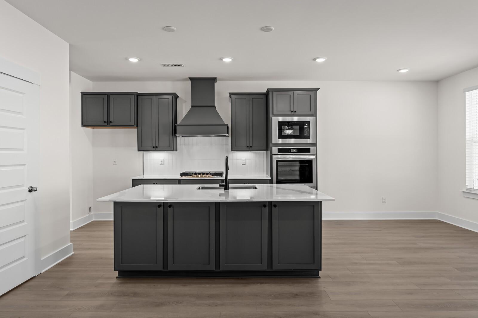 Modern kitchen with dark gray cabinets, white quartz island, and stainless appliances in The Willow at Woods Crossing.