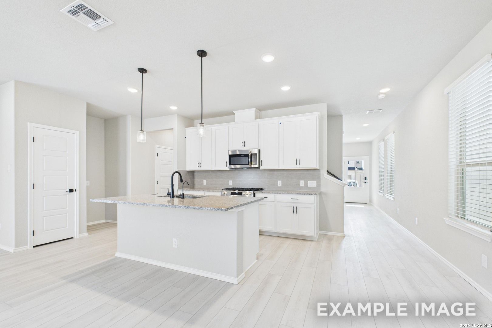 Modern kitchen with white cabinets, granite island, and pendant lighting in The Charlotte B plan at Cedar Heights, TX.